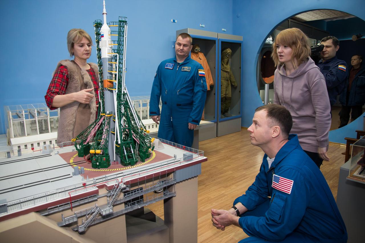 In the city of Baikonur, Kazakhstan, Expedition 55 backup crewmembers Alexey Ovchinin of Roscosmos (second from left) and Nick Hague of NASA (crouching) receive a briefing on the elements of a Soyuz rocket model March 6 during a traditional tour of the cit
