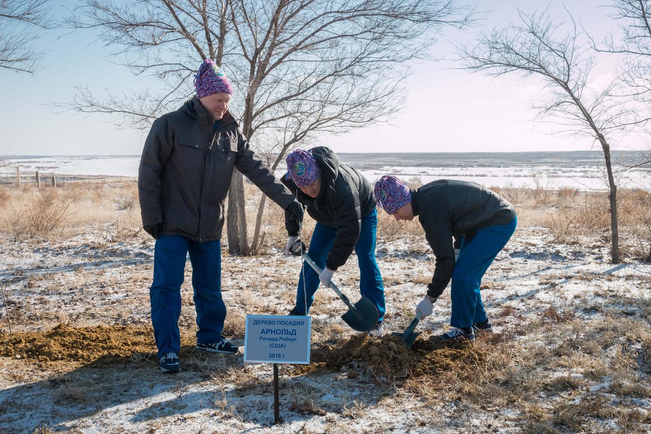 jsc2018e025542 - At the Cosmonaut Hotel crew quarters in Baikonur, Kazakhstan, Expedition 55 crewmember Ricky Arnold of NASA (center) plants a tree in his name March 15 in traditional pre-launch activities. Assisting him are his crewmates, Oleg Artemyev of Roscosmos (left) and Drew Feustel of NASA (right). They will launch March 21 on the Soyuz MS-08 spacecraft from the Baikonur Cosmodrome on a five-month mission to the International Space Station...NASA/Victor Zelentsov.