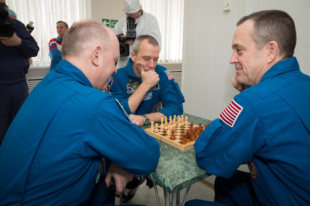 jsc2018e025551 - At the Cosmonaut Hotel crew quarters in Baikonur, Kazakhstan, Expedition 55 crewmembers Oleg Artemyev of Roscosmos (left), Drew Feustel of NASA (center) and Ricky Arnold of NASA (right) share a game of chess March 15 as part of their pre-launch activities. They will launch March 21 on the Soyuz MS-08 spacecraft from the Baikonur Cosmodrome on a five-month mission to the International Space Station...NASA/Victor Zelentsov.