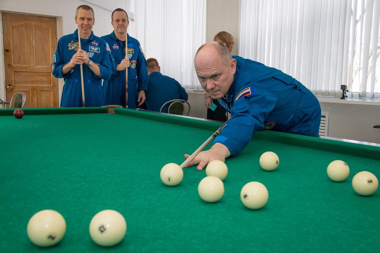 jsc2018e025552 - At the Cosmonaut Hotel crew quarters in Baikonur, Kazakhstan, Expedition 55 crewmember Oleg Artemyev of Roscosmos tries his hand at billiards March 15 as his crewmates, Drew Feustel of NASA (left) and Ricky Arnold of NASA (right) look on. They will launch March 21 on the Soyuz MS-08 spacecraft from the Baikonur Cosmodrome on a five-month mission to the International Space Station...NASA/Victor Zelentsov.