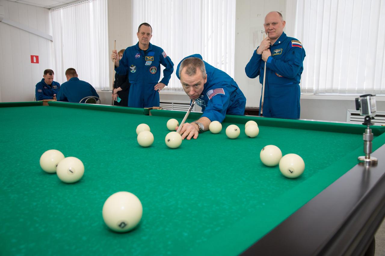 jsc2018e025553 - At the Cosmonaut Hotel crew quarters in Baikonur, Kazakhstan, Expedition 55 crewmember Drew Feustel of NASA tries his hand at billiards March 15 as his crewmates, Ricky Arnold of NASA (left) and Oleg Artemyev of Roscosmos (right) look on. In the background, backup crewmembers Nick Hague of NASA and Alexey Ovchinin of Roscosmos (back to camera) play a game of chess. Feustel, Arnold and Artemyev will launch March 21 on the Soyuz MS-08 spacecraft from the Baikonur Cosmodrome on a five-month mission to the International Space Station...NASA/Victor Zelentsov.
