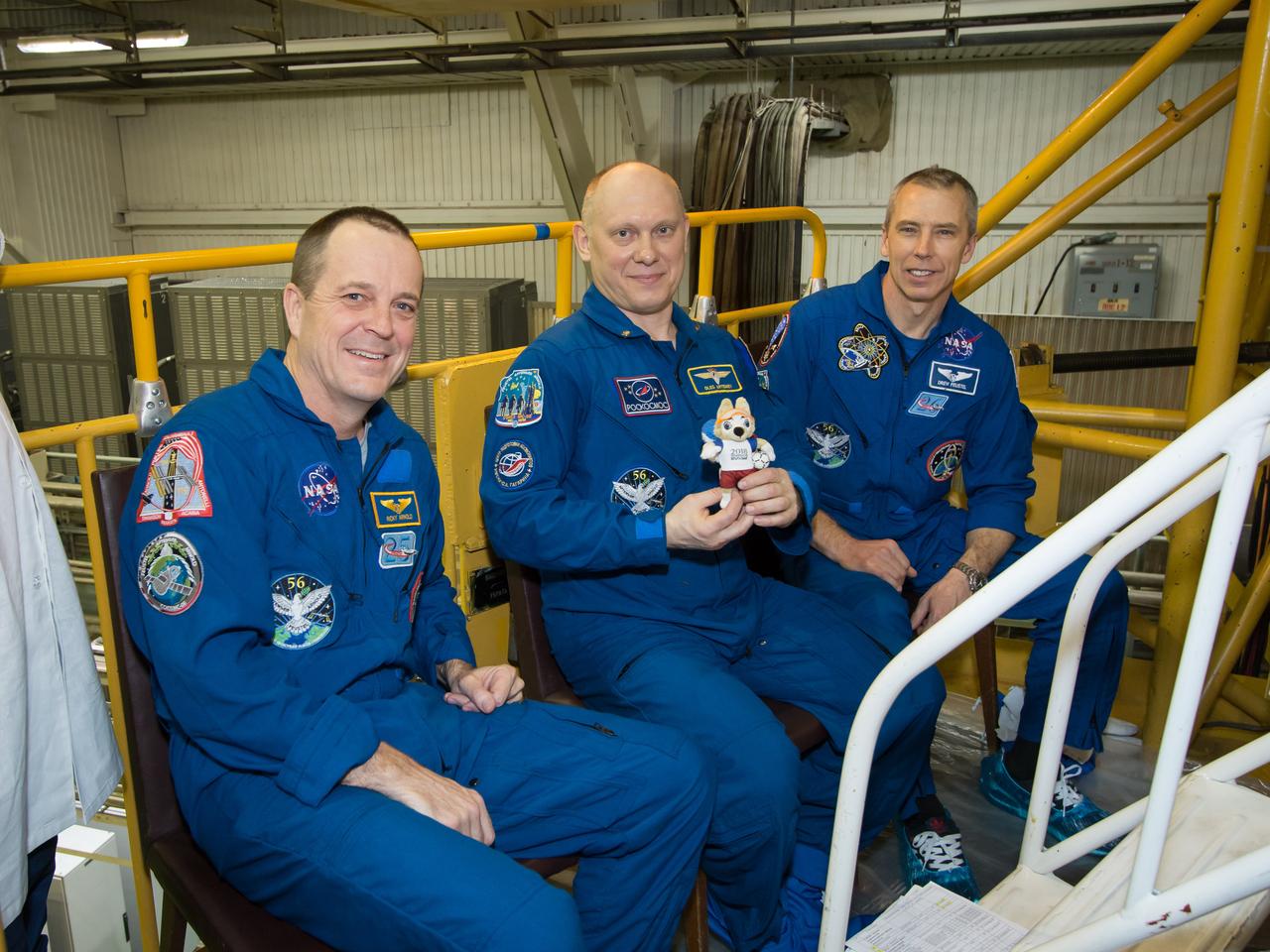 jsc2018e025588 - At the Baikonur Cosmodrome in Kazakhstan, Expedition 55 crewmember Oleg Artemyev of Roscosmos (center) holds a toy bear March 16 during Soyuz final fit check activities. The toy is one of several “zero gravity” mascots that will hang over the crew’s heads in the Soyuz during the vehicle’s ascent to orbit. Flanking Artemyev are his crewmates, Ricky Arnold of NASA (left) and Drew Feustel of NASA (right), who will launch March 21 on the Soyuz MS-08 spacecraft for a five-month mission on the International Space Station...NASA/Victor Zelentsov.