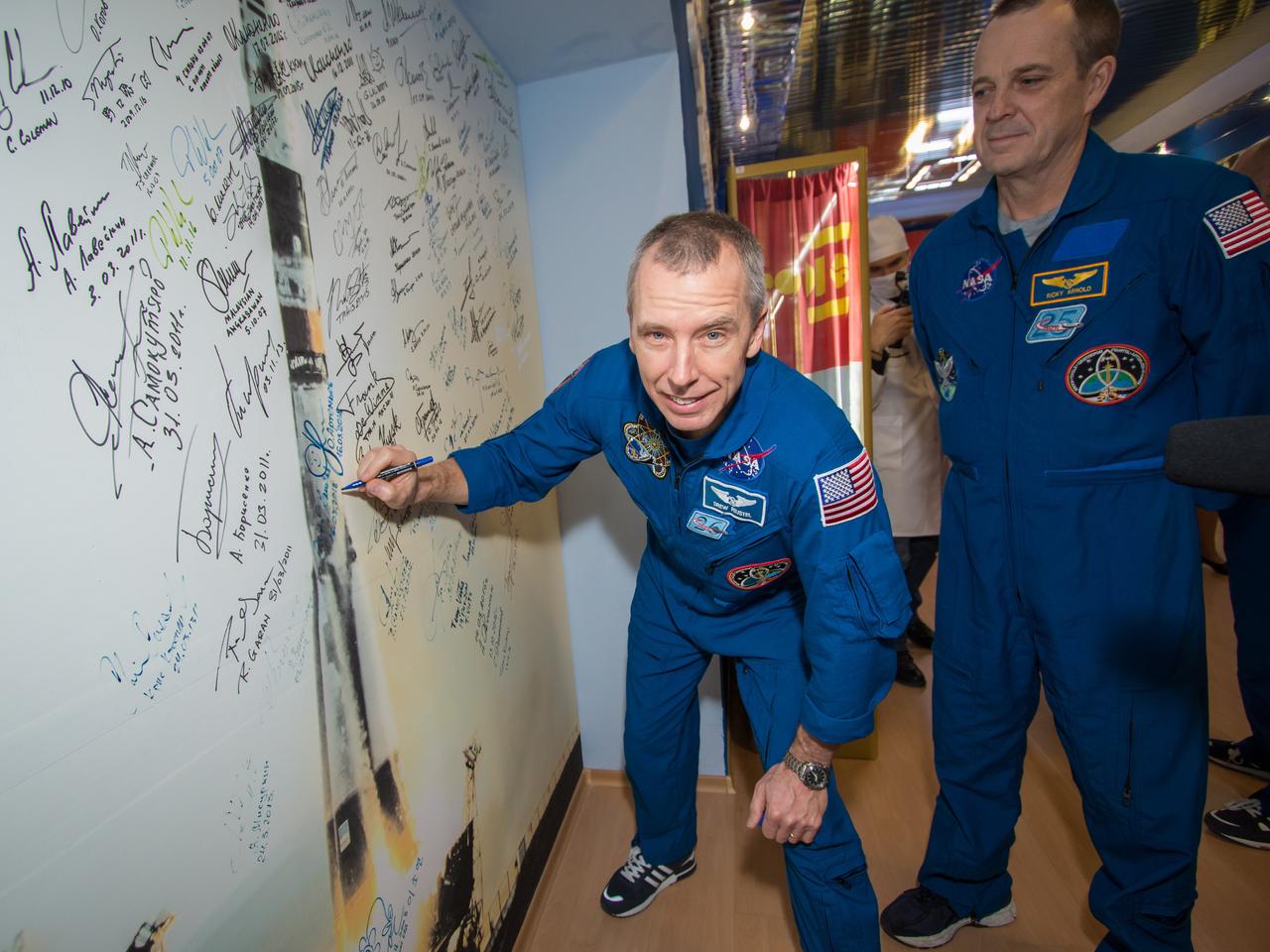 jsc2018e025591 - In the Korolev Museum at the Baikonur Cosmodrome in Kazakhstan, Expedition 55 crewmember Drew Feustel of NASA (left) signs a wall mural depicting a Soyuz launch March 16 as part of traditional prelaunch activities. Looking on is NASA crewmate Ricky Arnold (right). Along with Oleg Artemyev of Roscosmos, they will launch March 21 on the Soyuz MS-08 spacecraft for a five-month mission on the International Space Station...NASA/Victor Zelentsov.