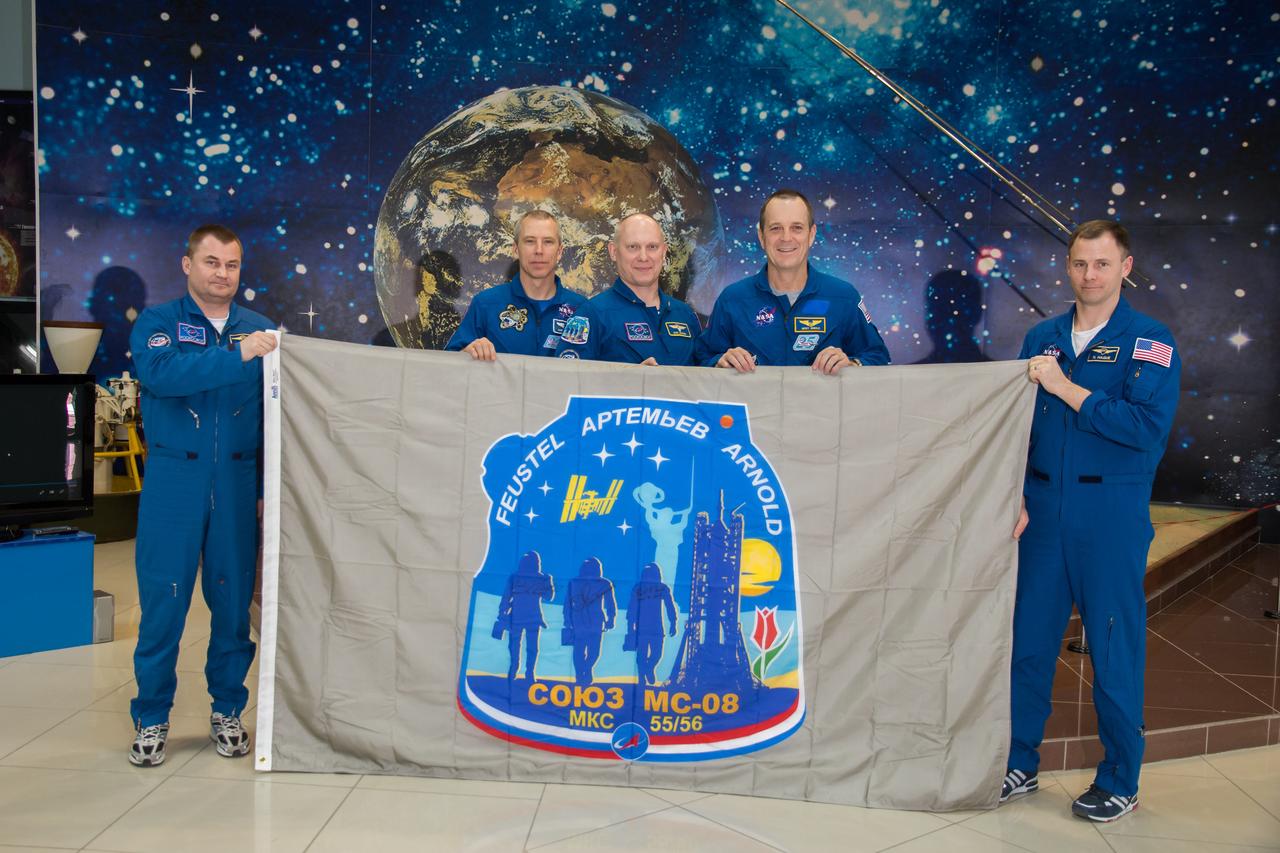 jsc2018e025596 - In the Korolev Museum at the Baikonur Cosmodrome in Kazakhstan, the Expedition 55 prime and backup crewmembers display a flag March 16 bearing the Soyuz MS-08 crew patch insignia during a traditional preflight tour of the museum. From left to right are backup crewmember Alexey Ovchinin of Roscosmos, prime crewmembers Drew Feustel of NASA, Oleg Artemyev of Roscosmos and Ricky Arnold of NASA, and backup crewmember Nick Hague of NASA. Feustel, Artemyev and Arnold will launch March 21 on the Soyuz MS-08 spacecraft for a five-month mission on the International Space Station...NASA/Victor Zelentsov.