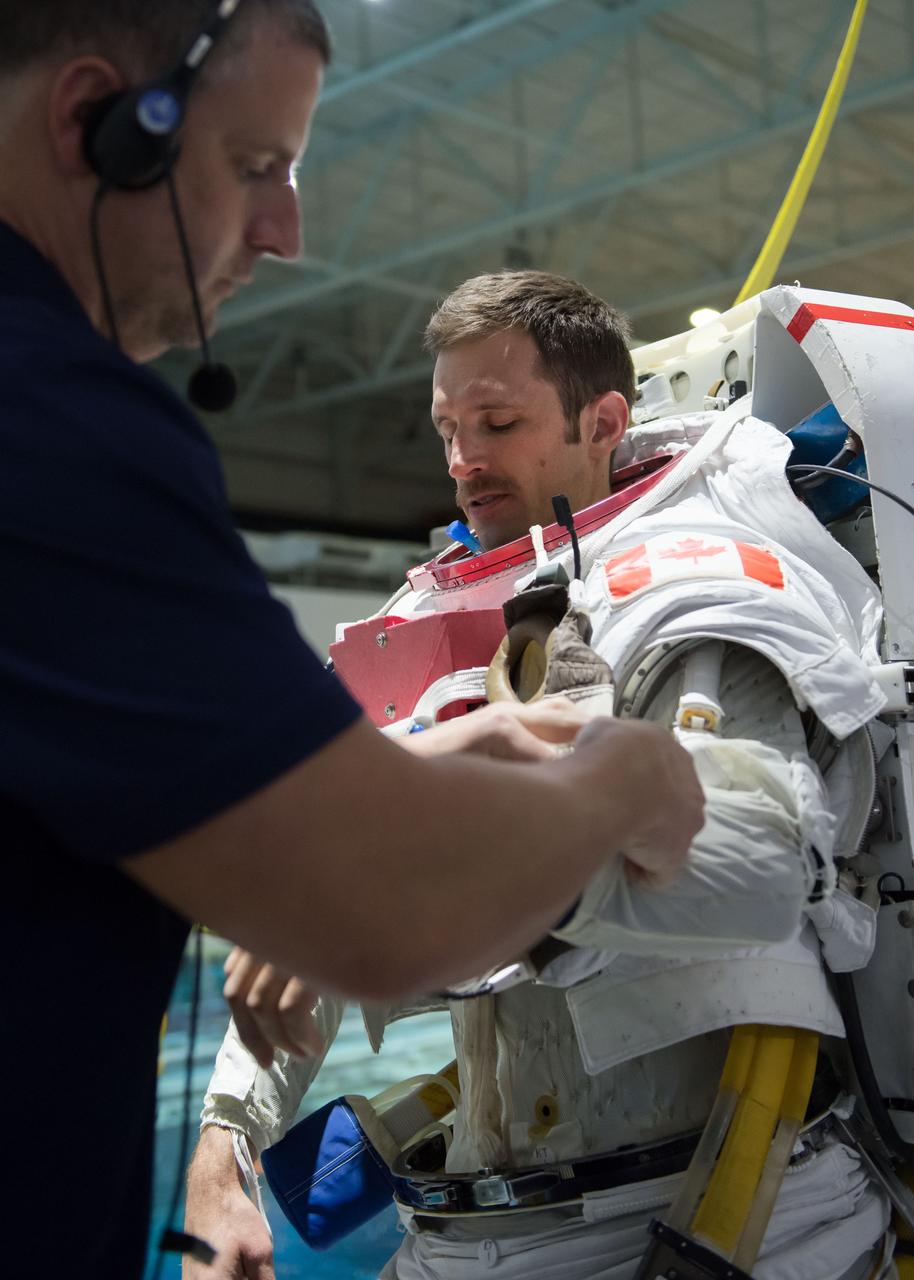 jsc2018e035767 (04-12-2018) --- 2017 Canadian Space Agency  astronaut candidate Joshua Kutryk is being helped into a spacesuit prior to underwater spacewalk training at NASA Johnson Space Center’s Neutral Buoyancy Laboratory. Photo Credit: (NASA/David DeHoyos)