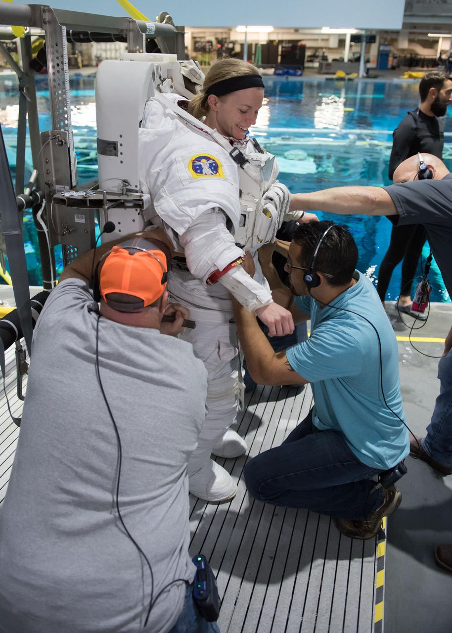 jsc2018e035771 (04-12-2018) --- NASA astronaut candidate Zena Cardman is being helped into a spacesuit prior to underwater spacewalk training at NASA Johnson Space Center’s Neutral Buoyancy Laboratory. Photo Credit: (NASA/David DeHoyos)
