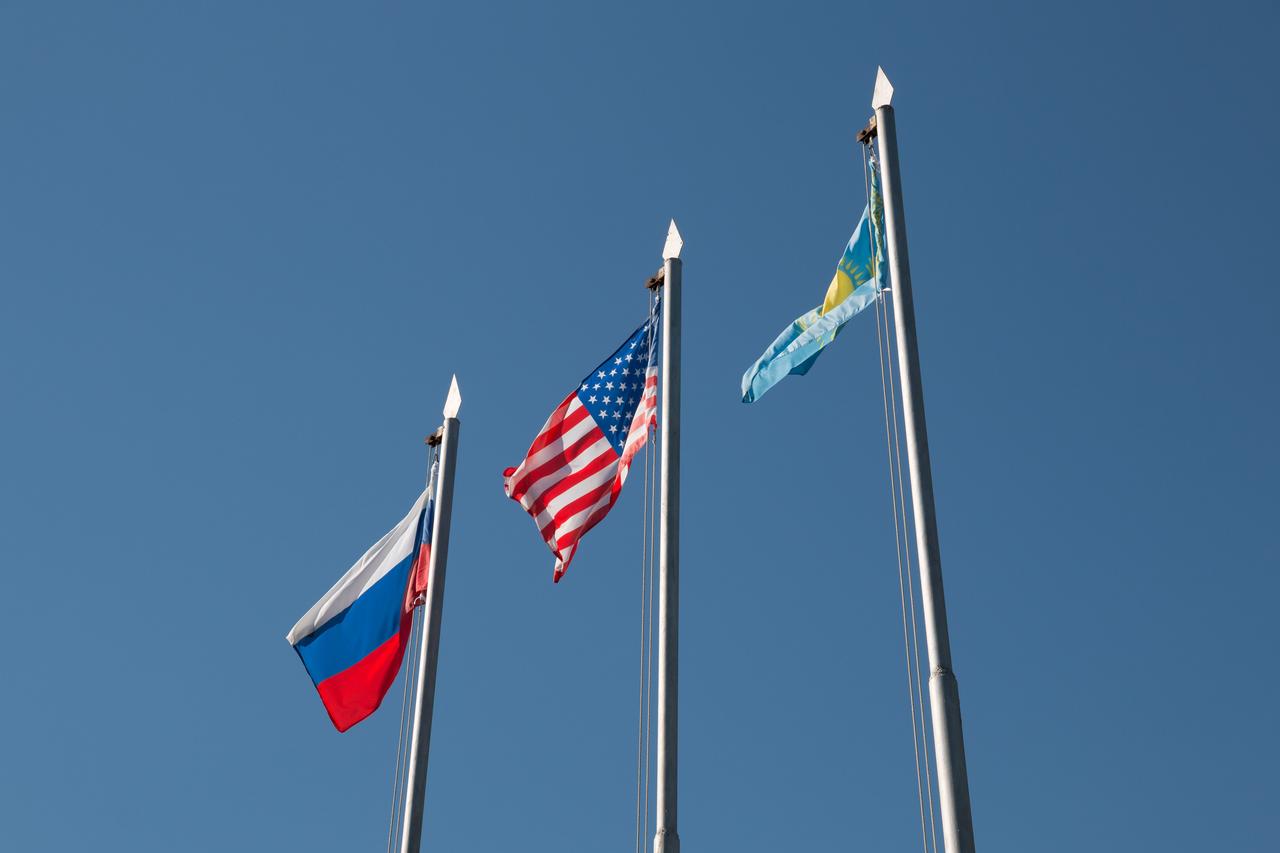 jsc2018e084636 - The flags of Russia, the United States and Kazakhstan fly high Sept. 27 at the Cosmonaut Hotel crew quarters in Baikonur, Kazakhstan after traditional flag-raising ceremonies. The flag-raising sets the stage for final pre-launch training for Alexey Ovchinin of Roscosmos and Nick Hague of NASA, who will launch Oct. 11 on the Soyuz MS-10 spacecraft from the Baikonur Cosmodrome in Kazakhstan for a six-month mission on the International Space Station...NASA/Victor Zelentsov.