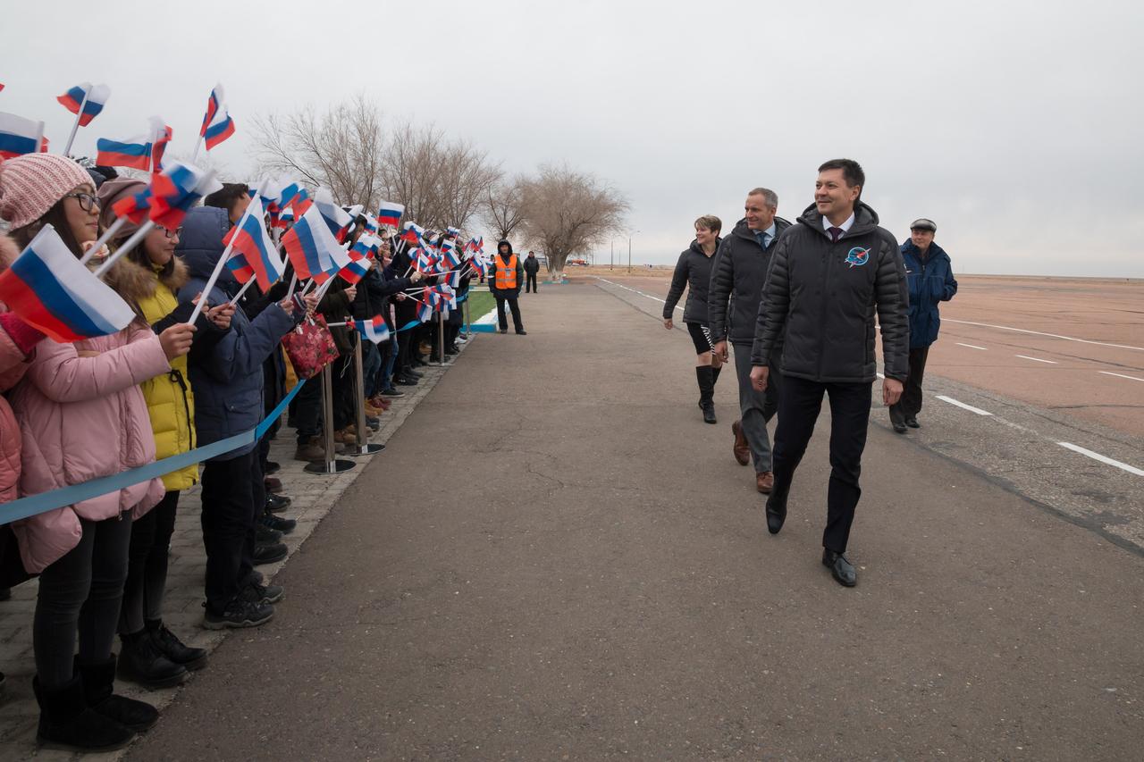 jsc2018e097264 - Expedition 58 crewmembers Anne McClain of NASA (top), Oleg Kononenko of Roscosmos (center) and David Saint-Jacques of the Canadian Space Agency (foreground) are greeted by local school children Nov. 19 after arriving at their launch site in Baikonur, Kazakhstan for final pre-launch training. They will launch Dec. 3 on the Soyuz MS-11 spacecraft from the Baikonur Cosmodrome in Kazakhstan for a six-and-a-half month mission on the International Space Station...NASA/Victor Zelentsov.