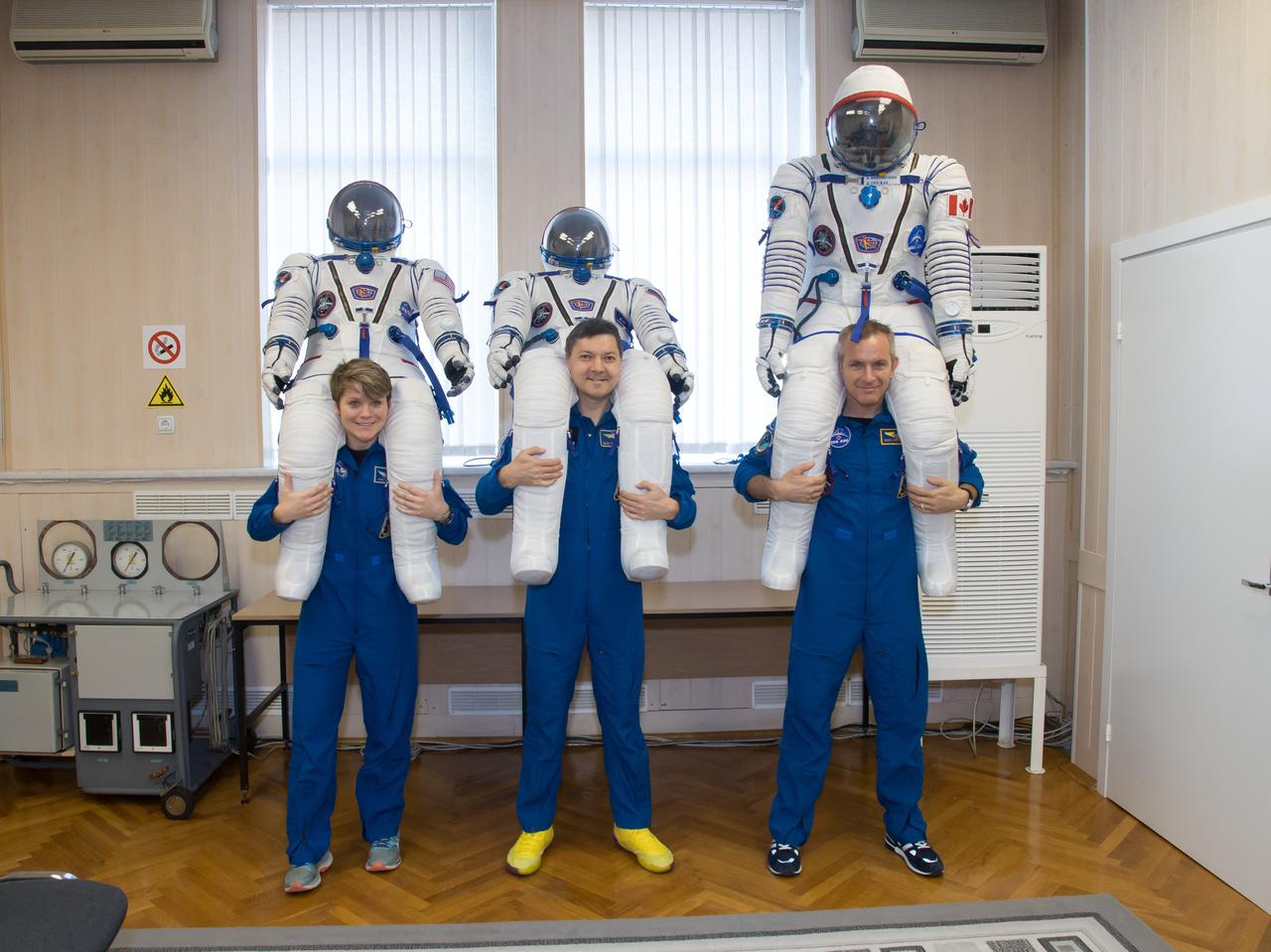 jsc2018e097307 - In the Integration Facility at the Baikonur Cosmodrome in Kazakhstan, Expedition 58 crewmembers Anne McClain of NASA, Oleg Kononenko of Roscosmos (center) and David Saint-Jacques of the Canadian Space Agency pose for pictures with their Russian Sokol launch and entry suits Nov. 20 during a vehicle fit check. They will launch Dec. 3 on the Soyuz MS-11 spacecraft from the Baikonur Cosmodrome for a six-and-a-half month mission on the International Space Station...NASA/Victor Zelentsov.