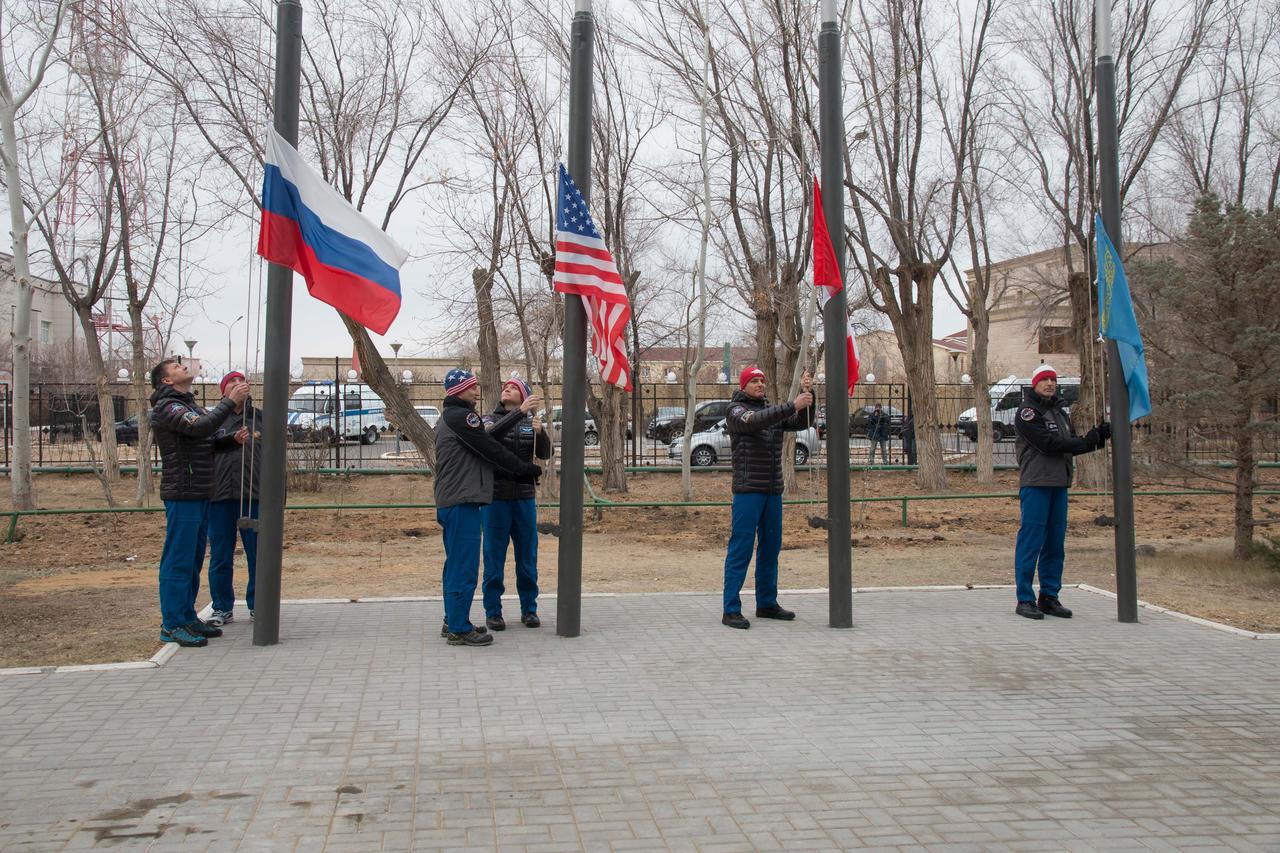 jsc2018e097309 - Outside the Cosmonaut Hotel crew quarters in Baikonur, Kazakhstan, the Expedition 58 prime and backup crewmembers raise the flags of Russia, the United States, Canada and Kazakhstan Nov. 21 in a traditional ceremony. Anne McClain of NASA, Oleg Kononenko of Roscosmos and David Saint-Jacques of the Canadian Space Agency will launch Dec. 3 on the Soyuz MS-11 spacecraft from the Baikonur Cosmodrome in Kazakhstan for a six-and-a-half month mission on the International Space Station...NASA/Victor Zelentsov.