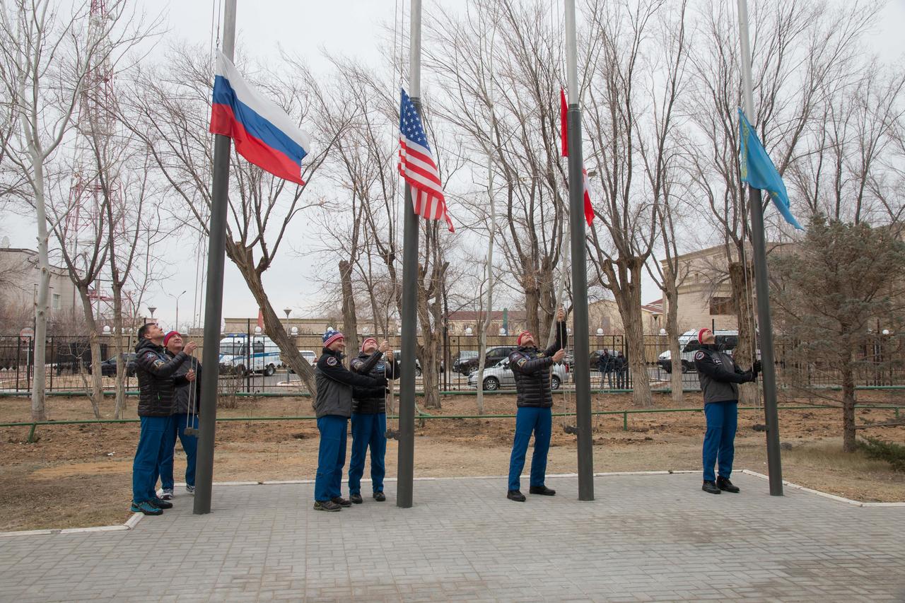 jsc2018e097310 - Outside the Cosmonaut Hotel crew quarters in Baikonur, Kazakhstan, the Expedition 58 prime and backup crewmembers raise the flags of Russia, the United States, Canada and Kazakhstan Nov. 21 in a traditional ceremony. Anne McClain of NASA, Oleg Kononenko of Roscosmos and David Saint-Jacques of the Canadian Space Agency will launch Dec. 3 on the Soyuz MS-11 spacecraft from the Baikonur Cosmodrome in Kazakhstan for a six-and-a-half month mission on the International Space Station...NASA/Victor Zelentsov.