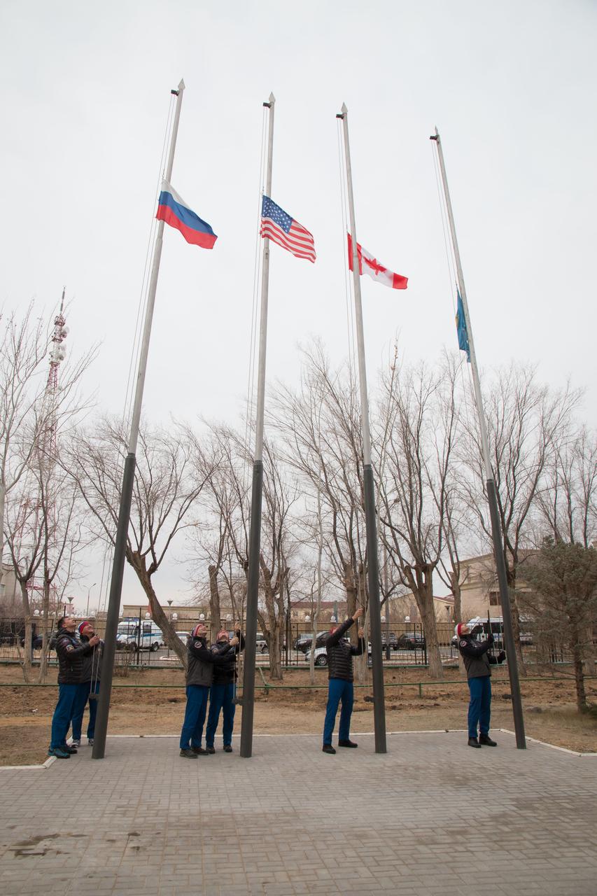 jsc2018e097311 - Outside the Cosmonaut Hotel crew quarters in Baikonur, Kazakhstan, the Expedition 58 prime and backup crewmembers raise the flags of Russia, the United States, Canada and Kazakhstan Nov. 21 in a traditional ceremony. Anne McClain of NASA, Oleg Kononenko of Roscosmos and David Saint-Jacques of the Canadian Space Agency will launch Dec. 3 on the Soyuz MS-11 spacecraft from the Baikonur Cosmodrome in Kazakhstan for a six-and-a-half month mission on the International Space Station...NASA/Victor Zelentsov.