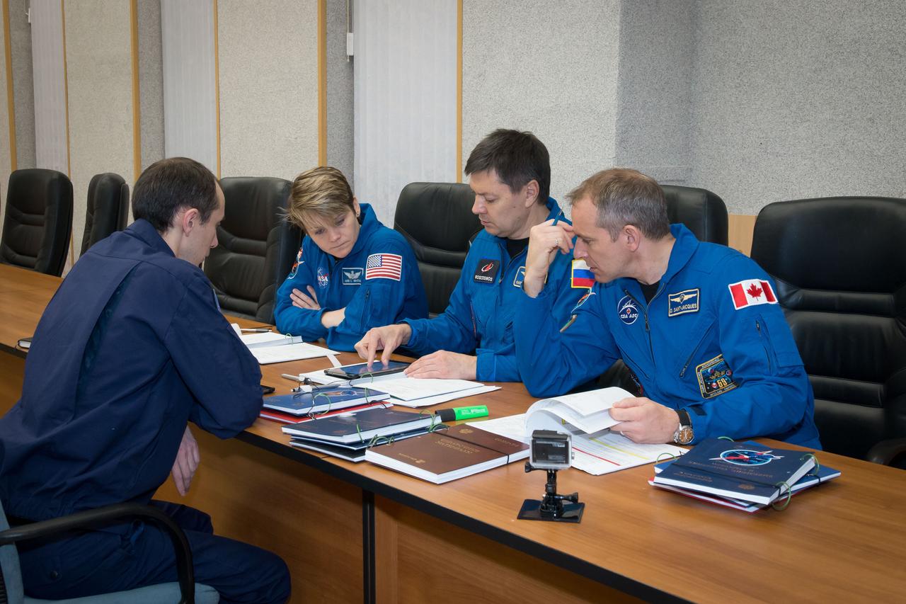 jsc2018e097766 - At their Cosmonaut Hotel crew quarters in Baikonur, Kazakhstan, Expedition 58 crewmembers Anne McClain of NASA (left), Oleg Kononenko of Roscosmos (center) and David Saint-Jacques (right) review flight procedures with a training instructor Nov. 27 as part of their pre-launch training. They will launch Dec. 3 on the Soyuz MS-11 spacecraft from the Baikonur Cosmodrome in Kazakhstan for a six-and-a-half month mission on the International Space Station...NASA/Victor Zelentsov.