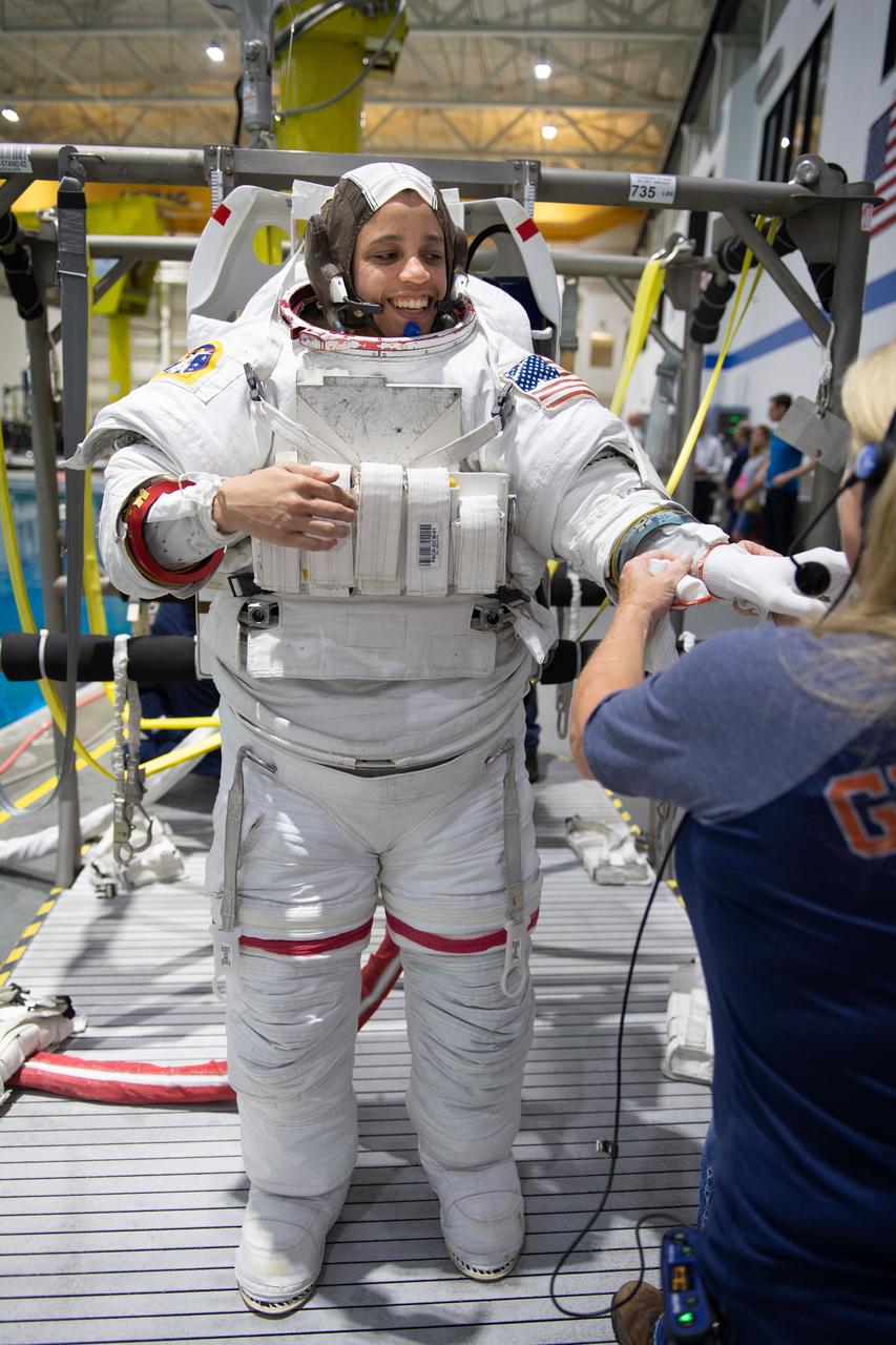 jsc2019e030025 (05-22-19) --- 2017 NASA astronaut candidate Jessica Watkins is helped into a spacesuit prior to underwater spacewalk training at NASA Johnson Space Center’s Neutral Buoyancy Laboratory in Houston. Photo Credit: (NASA/David DeHoyos)