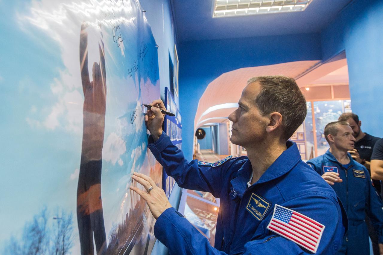 jsc2019e038394 - At the Baikonur Museum in the town of Baikonur, Kazakhstan, Expedition 60 backup crewmember Tom Marshburn of NASA signs a wall mural July 6 during traditional pre-launch activities. In the background is crewmate Sergey Ryzhikov of Roscosmos. Marshburn, Ryzhikov and Soichi Noguchi of the Japan Aerospace Exploration Agency are the backups to the prime crew, Drew Morgan of NASA, Luca Parmitano of the European Space Agency and Alexander Skvortsov of Roscosmos, who will launch July 20 on the Soyuz MS-13 spacecraft from the Baikonur Cosmodrome in Kazakhstan for a mission on the International Space Station...Andrey Shelepin/GCTC.