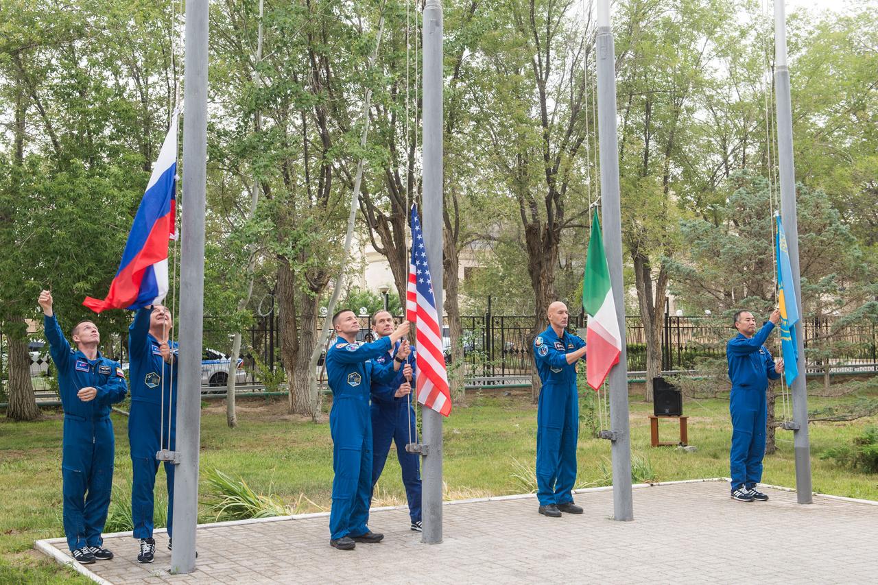 jsc2019e038395 - At their Cosmonaut Hotel crew quarters in Baikonur, Kazakhstan, Expedition 60 prime and backup crewmembers Sergey Ryzhikov and Alexander Skvortsov of Roscosmos, Drew Morgan and Tom Marshburn of NASA, Luca Parmitano of the European Space Agency and Soichi Noguchi of the Japan Aerospace Exploration Space Agency raise the flags of Russia, the United States, Italy and Kazakhstan in a traditional ceremony July 6. Morgan, Parmitano and Skvortsov will launch July 20 on the Soyuz MS-13 spacecraft from the Baikonur Cosmodrome in Kazakhstan for a mission on the International Space Station...Andrey Shelepin/GCTC.