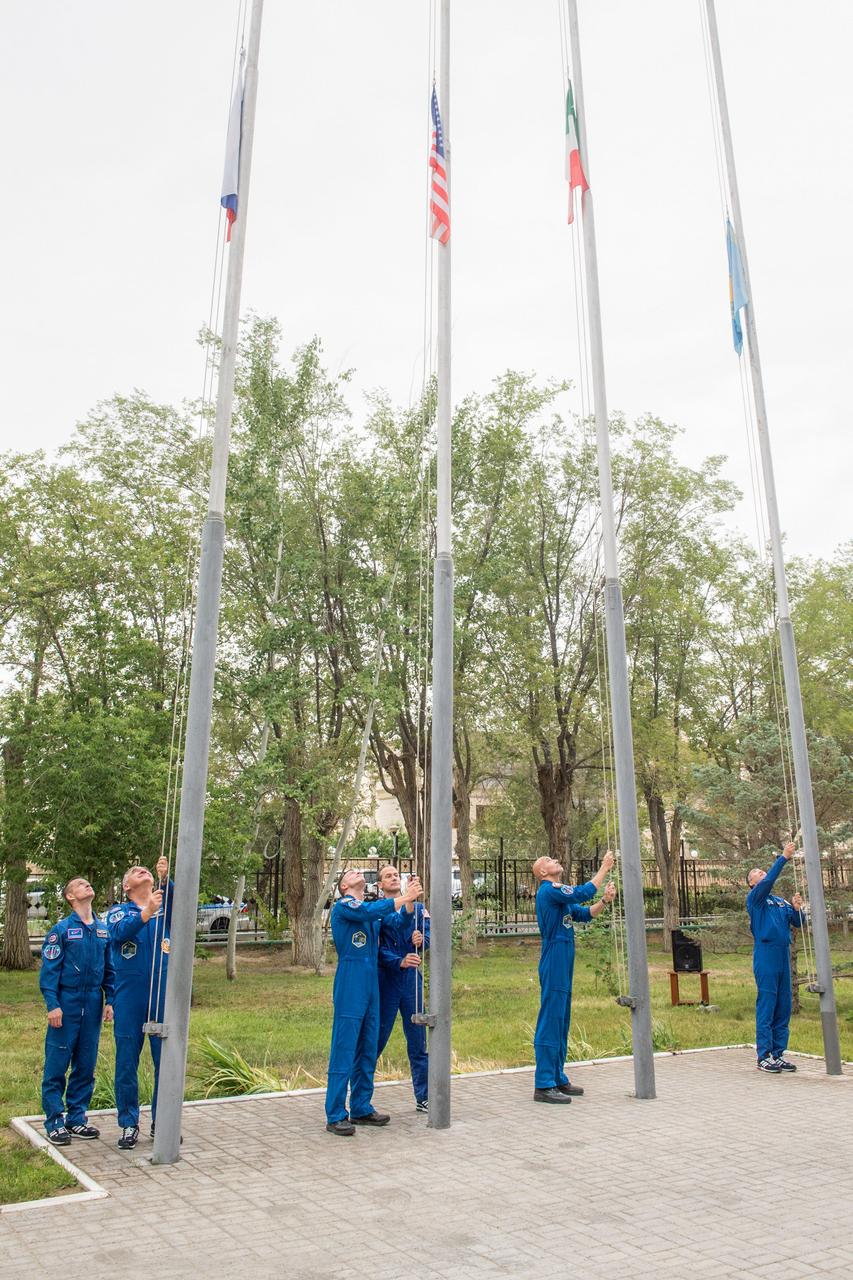 jsc2019e038396 - At their Cosmonaut Hotel crew quarters in Baikonur, Kazakhstan, Expedition 60 prime and backup crewmembers Sergey Ryzhikov and Alexander Skvortsov of Roscosmos, Drew Morgan and Tom Marshburn of NASA, Luca Parmitano of the European Space Agency and Soichi Noguchi of the Japan Aerospace Exploration Space Agency raise the flags of Russia, the United States, Italy and Kazakhstan in a traditional ceremony July 6. Morgan, Parmitano and Skvortsov will launch July 20 on the Soyuz MS-13 spacecraft from the Baikonur Cosmodrome in Kazakhstan for a mission on the International Space Station...Andrey Shelepin/GCTC.