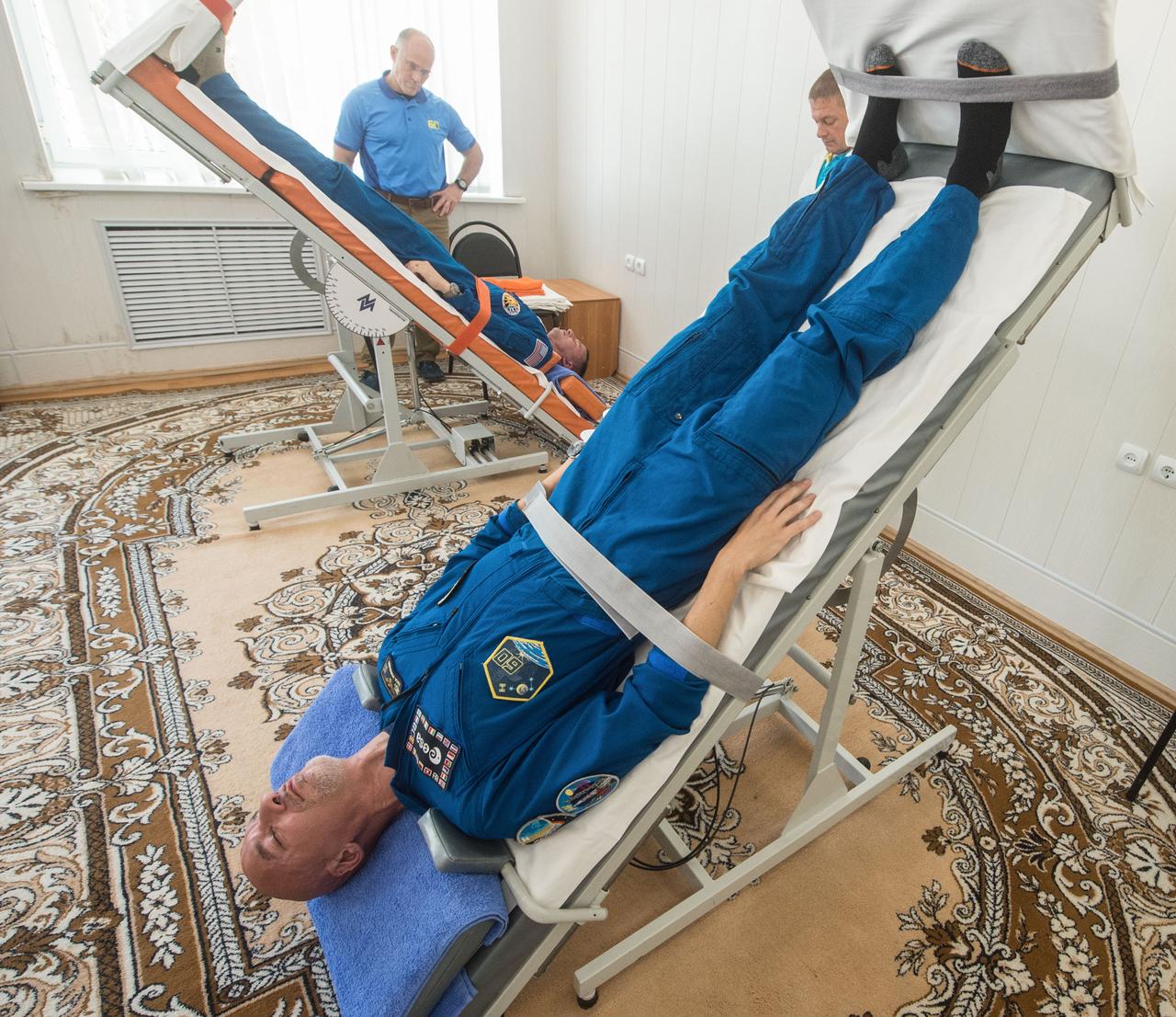 jsc2019e039266 - At the Cosmonaut Hotel crew quarters in Baikonur, Kazakhstan, Expedition 60 crewmembers Luca Parmitano of the European Space Agency (foreground) and Drew Morgan of NASA test out their vestibular systems on tilt tables July 12 as part of pre-launch activities. Along with Alexander Skvortsov of Roscosmos, they will launch July 20 on the Soyuz MS-13 spacecraft from the Baikonur Cosmodrome in Kazakhstan on a mission to the International Space Station...Andrey Shelepin/GCTC.