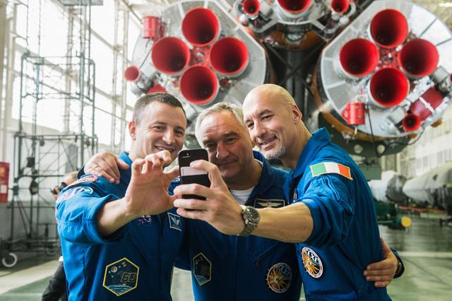 jsc2019e039431 - In the Integration Building at the Baikonur Cosmodrome in Kazakhstan, Expedition 60 crewmembers Drew Morgan of NASA (left), Alexander Skvortsov of Roscosmos (center) and Luca Parmitano of the European Space Agency (right) pose for a selfie in front of the first stage engines of their Soyuz booster July 16 as part of pre-launch preparations. They will launch July 20 on the Soyuz MS-13 spacecraft from the Baikonur Cosmodrome for a mission on the International Space Station...Andrey Shelepin/GCTC.