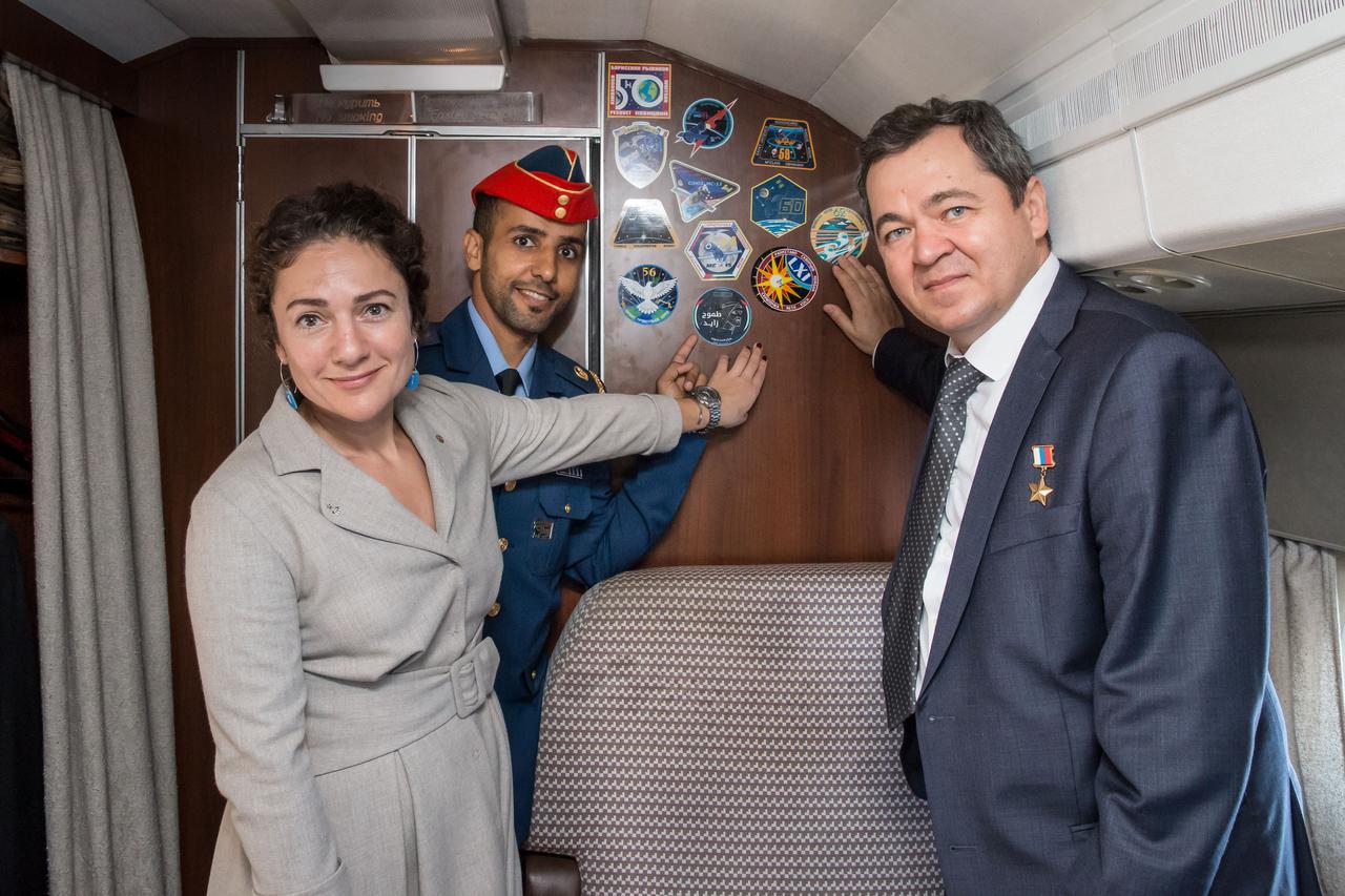 jsc2019e052741 - Aboard a Gagarin Cosmonaut Training Center aircraft, Expedition 61 crewmembers Jessica Meir of NASA (left) and Oleg Skripochka of Roscosmos (right) and spaceflight participant Hazzaa Ali Amansoori of the United Arab Emirates (center) point to stickers bearing their mission's insignias Sept. 10 as they flew from their training base in Star City, Russia to their launch site at the Baikonur Cosmodrome in Kazakhstan. They will launch on Sept. 25 from the Baikonur Cosmodrome on the Soyuz MS-15 spacecraft for a mission on the International Space Station...NASA/Victor Zelentsov