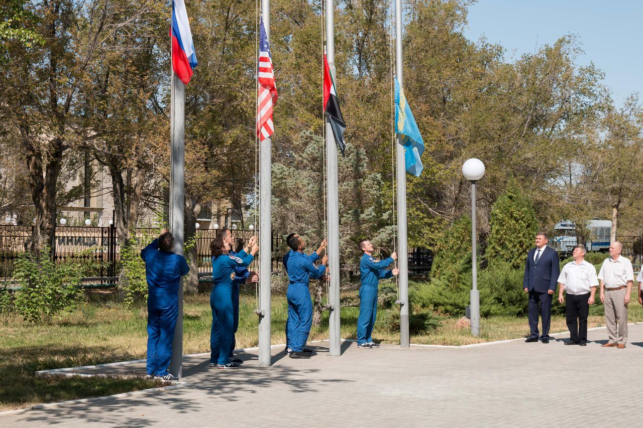 jsc2019e052901 - At their Cosmonaut Hotel crew quarters in Baikonur, Kazakhstan, the prime and backup crewmembers for the next launch to the International Space Station raise the flags of Russia, the United States, the United Arab Emirates and Kazakhstan Sept. 12 in a traditional ceremony. Expedition 61 crewmembers Oleg Skripochka of Roscosmos and Jessica Meir of NASA and spaceflight participant Hazzaa Ali Almansoori of the United Arab Emirates will launch Sept. 25 on the Soyuz MS-15 spacecraft for a mission on the International Space Station...NASA/Victor Zelentsov.