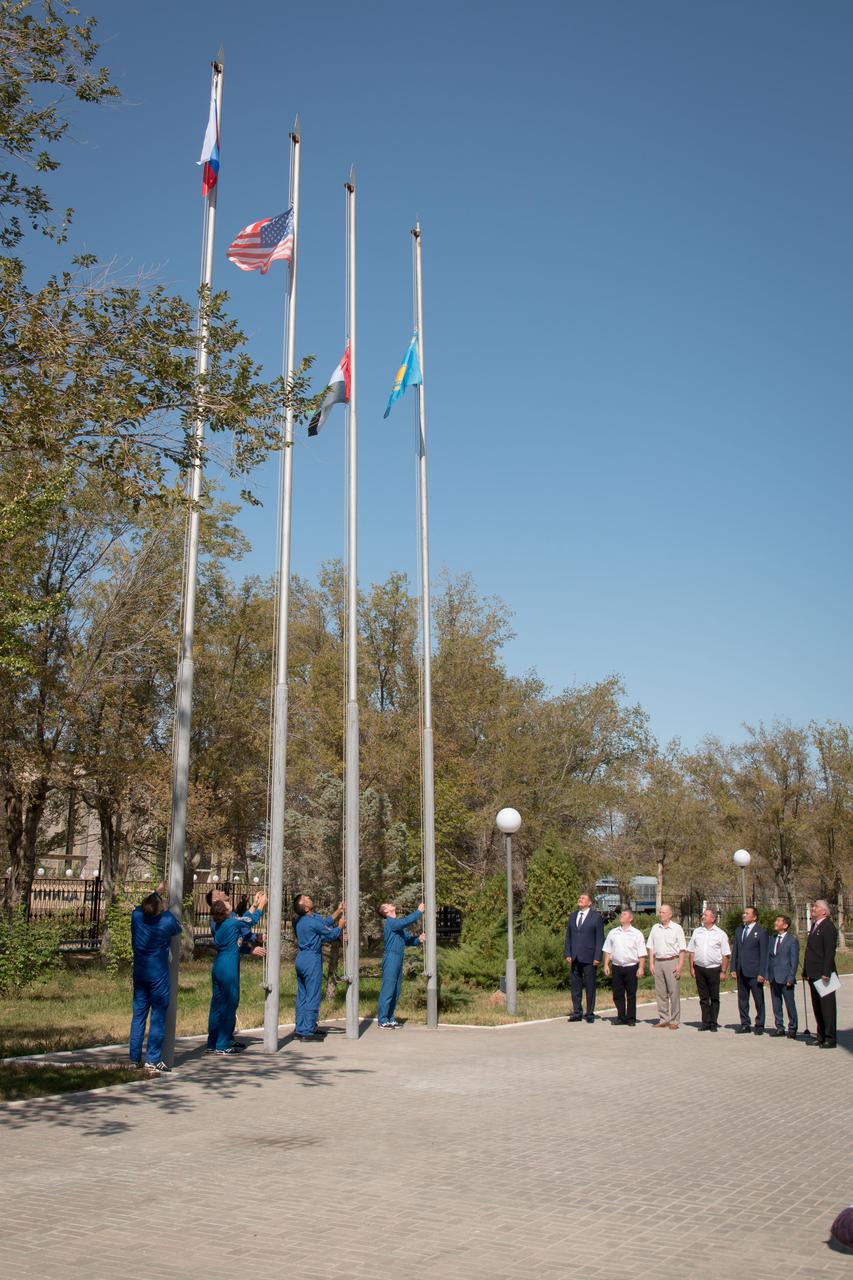 jsc2019e052902 - At their Cosmonaut Hotel crew quarters in Baikonur, Kazakhstan, the prime and backup crewmembers for the next launch to the International Space Station raise the flags of Russia, the United States, the United Arab Emirates and Kazakhstan Sept. 12 in a traditional ceremony. Expedition 61 crewmembers Oleg Skripochka of Roscosmos and Jessica Meir of NASA and spaceflight participant Hazzaa Ali Almansoori of the United Arab Emirates will launch Sept. 25 on the Soyuz MS-15 spacecraft for a mission on the International Space Station...NASA/Victor Zelentsov.