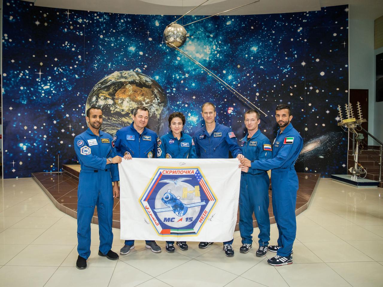 jsc2019e053741 - At the Baikonur Cosmodrome Museum in Kazakhstan, the prime and backup crewmembers for the next launch to the International Space Station display a flag bearing the insignia of their Soyuz mission Sept. 20 during pre-launch activities. From left to right are the prime crew, spaceflight participant Hazzaa ali Almansoori of the United Arab Emirates and Expedition 61 crewmembers Oleg Skripochka of Roscosmos and Jessica Meir of NASA and backup crewmembers Tom Marshburn of NASA, Sergey Ryzhikov of Roscosmos and Sultan Al-Neyadi of the United Arab Emirates. Meir, Skripochka and Almansoori will launch Sept. 25 on the Soyuz MS-15 spacecraft for a mission on the International Space Station...NASA/Victor Zelentsov