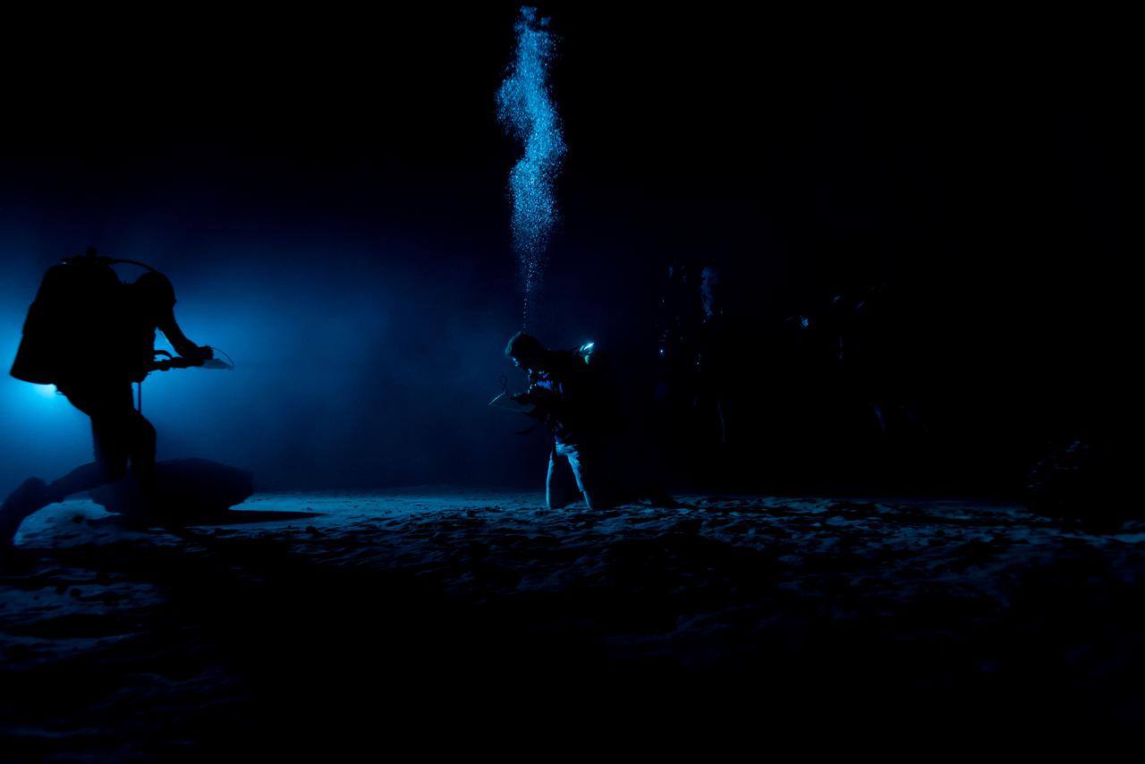 Test subjects performing subjective assessment of underwater lamp source during NBL Preliminary Lunar Lighting Evaluation.  Divers at the Neutral Buoyancy Laboratory (NBL) in Houston are setting the stage for future Moonwalk training by simulating lunar lighting conditions. At the Lunar South Pole, the Sun will remain no more than a few degrees above the horizon, resulting in extremely long and dark shadows. To prepare astronauts for these challenging lighting conditions, the team at the NBL has begun preliminary evaluations of lunar lighting solutions at the bottom of the 40-foot deep pool. This testing and evaluation involved turning off all the lights in the facility, installing black curtains on the pool walls to minimize reflections, and using a powerful underwater cinematic lamp, to get the conditions just right ahead of upcoming training for astronauts.