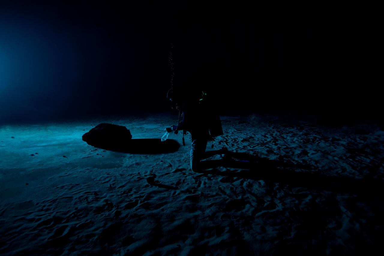 Test subjects performing subjective assessment of underwater lamp source during NBL Preliminary Lunar Lighting Evaluation.  Divers at the Neutral Buoyancy Laboratory (NBL) in Houston are setting the stage for future Moonwalk training by simulating lunar lighting conditions. At the Lunar South Pole, the Sun will remain no more than a few degrees above the horizon, resulting in extremely long and dark shadows. To prepare astronauts for these challenging lighting conditions, the team at the NBL has begun preliminary evaluations of lunar lighting solutions at the bottom of the 40-foot deep pool. This testing and evaluation involved turning off all the lights in the facility, installing black curtains on the pool walls to minimize reflections, and using a powerful underwater cinematic lamp, to get the conditions just right ahead of upcoming training for astronauts.