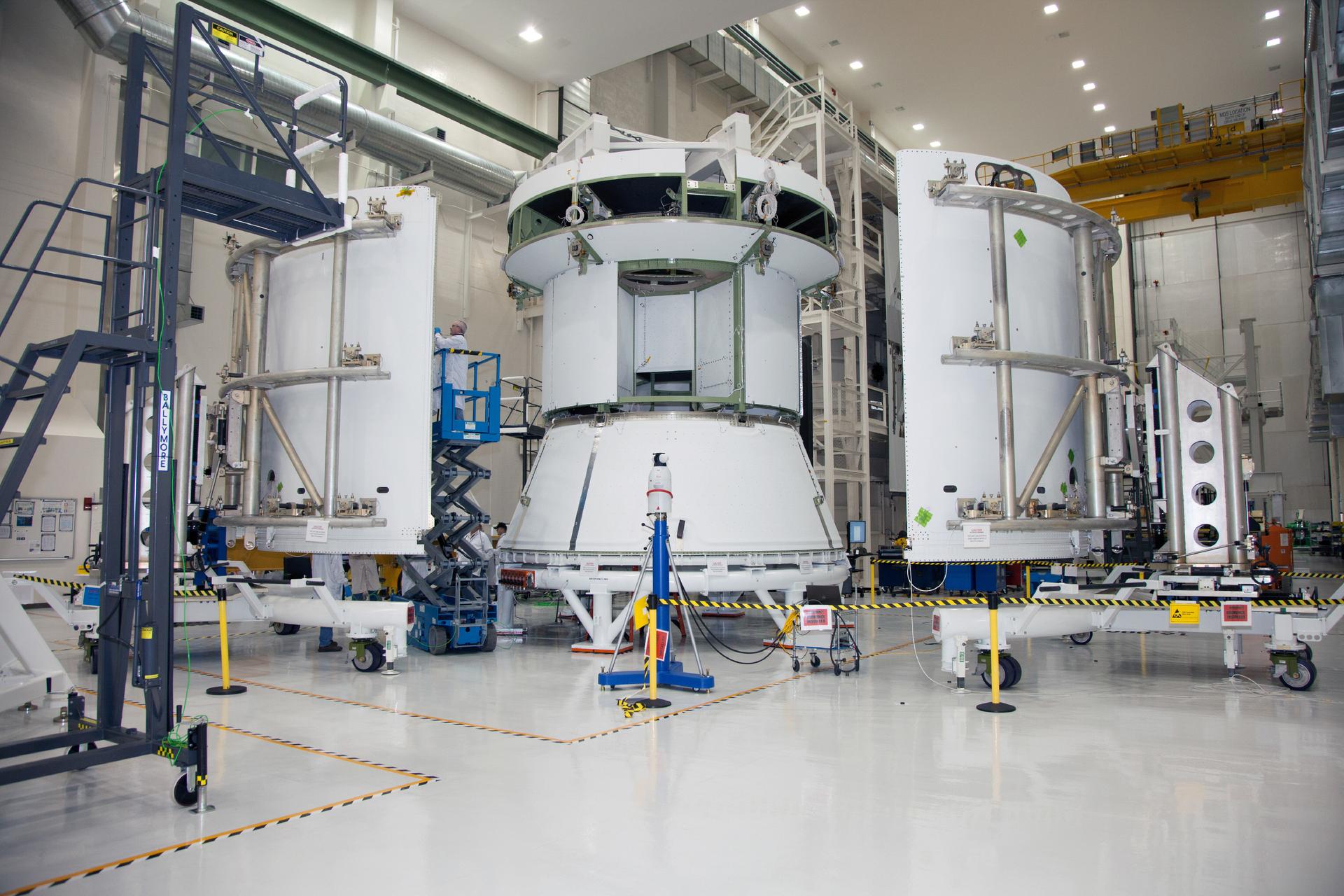 A technician on a scissor lift works on the service module for the Orion spacecraft.