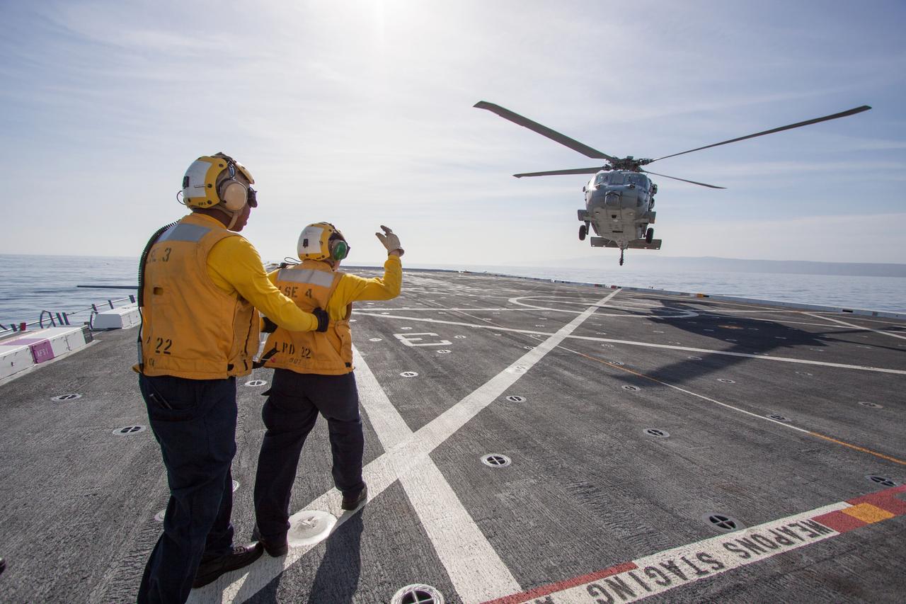 On the top deck of the USS San Diego, a helicopter flies overhead to monitor conditions as the Orion underway recovery test begins in the Pacific Ocean, about 100 miles off the coast of San Diego, California on Feb. 20, 2014. The Orion boilerplate test vehicle and other hardware are secured in the well deck of the ship in preparation for the test. NASA and the U.S. Navy conducted tests to prepare for the recovery of the Orion crew module, forward bay cover and parachutes on its return from a deep space mission. The underway recovery test will allow the teams to demonstrate and evaluate the recovery processes, procedures, hardware and personnel in open waters. Part of Batch image transfer from Flickr.
