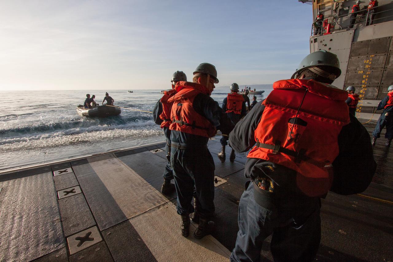 On the top deck of the USS San Diego, a helicopter flies overhead to monitor conditions as the Orion underway recovery test begins in the Pacific Ocean, about 100 miles off the coast of San Diego, California on Feb. 20, 2014. The Orion boilerplate test vehicle and other hardware are secured in the well deck of the ship in preparation for the test. NASA and the U.S. Navy conducted tests to prepare for the recovery of the Orion crew module, forward bay cover and parachutes on its return from a deep space mission. The underway recovery test will allow the teams to demonstrate and evaluate the recovery processes, procedures, hardware and personnel in open waters. Part of Batch image transfer from Flickr.