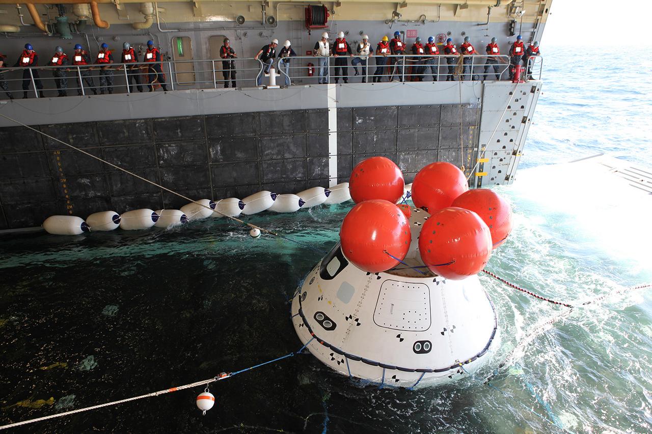 Recovery team members use ropes to hold a test version of Orion steady inside the USS Anchorage's well deck as it is reeled in from the Pacific Ocean on Sept. 17, 2014, during a test of tools and techniques that will be used to retrieve the spacecraft once it splashes down following Exploration Flight Test-1 (EFT-1). Part of Batch image transfer from Flickr.