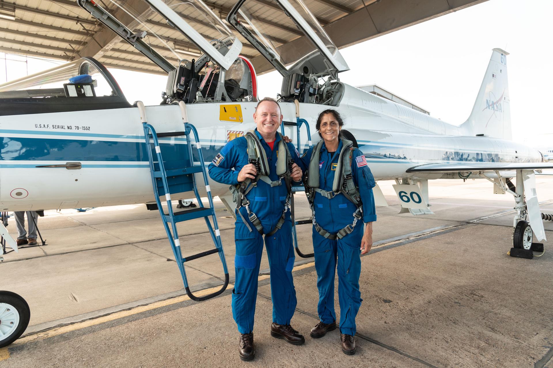 Two astronauts in their blue suits pose in front of a jet.