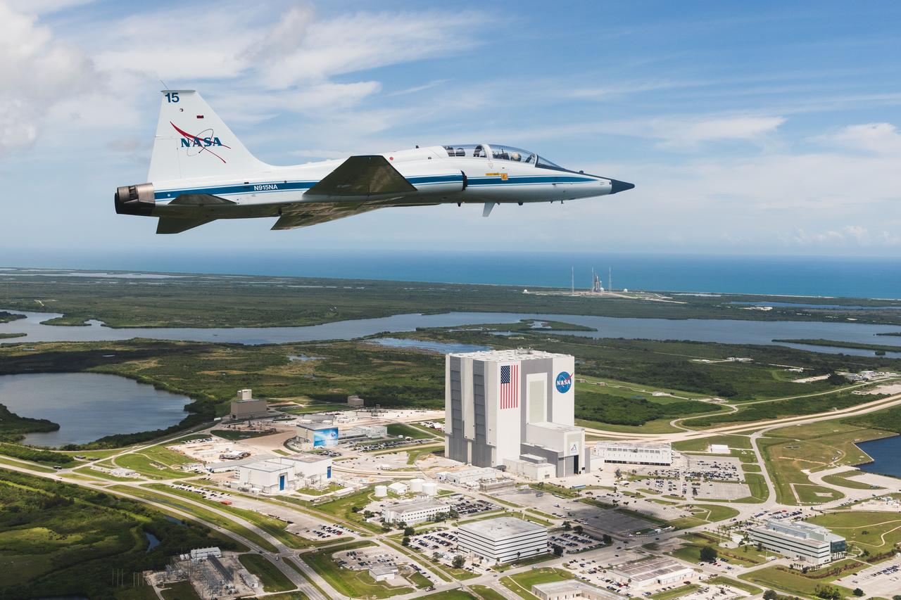 Pilot Chris 'Trigger" Condon and Astronaut Zena Cardman fly over NASA's Kennedy Space Center. The Vehicle Assembly Building is visible in the foreground with launch pads in the background. Credit: NASA/Josh Valcarcel