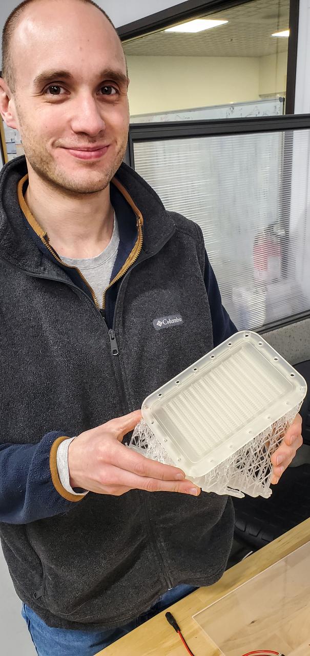 jsc2023e010171 (2/1/2023) --- Logan Torres, design engineer for the CapiSorb Visible System, holds the 3D printed degasser base during hardware fabrication. The capillary wedges in the degasser base control and passively transport viscous liquid in microgravity in order to demonstrate capabilities needed for future liquid sorbent carbon dioxide removal technologies. The CapiSorb Visible System investigation demonstrates a liquid control using capillary forces, over a range of properties that are characteristic of liquids which absorb carbon dioxide. Image courtesy of IRPI, LLC.