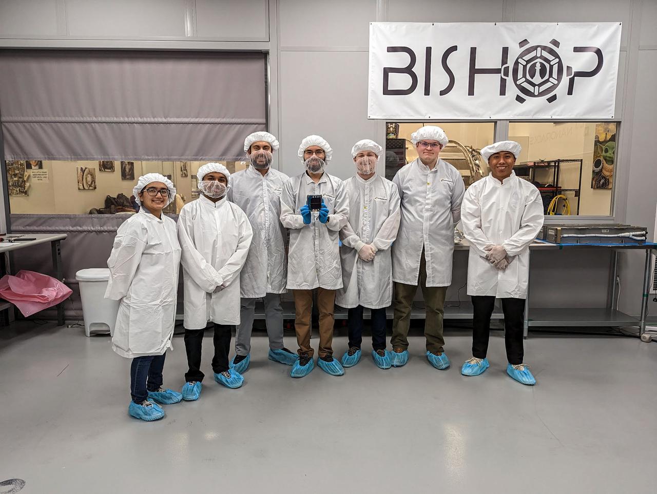 jsc2023e010187 (12/13/2022) --- LightCube team members with their CubeSat on integration day. From back to left to right: Ashley Lepham, Sam Cherian, Raymond Barakat, Jaime Sanchez de la Vega, Chandler Hutchens, Christopher McCormick, David Ordaz Perez. Image courtesy of Sam Cherian.