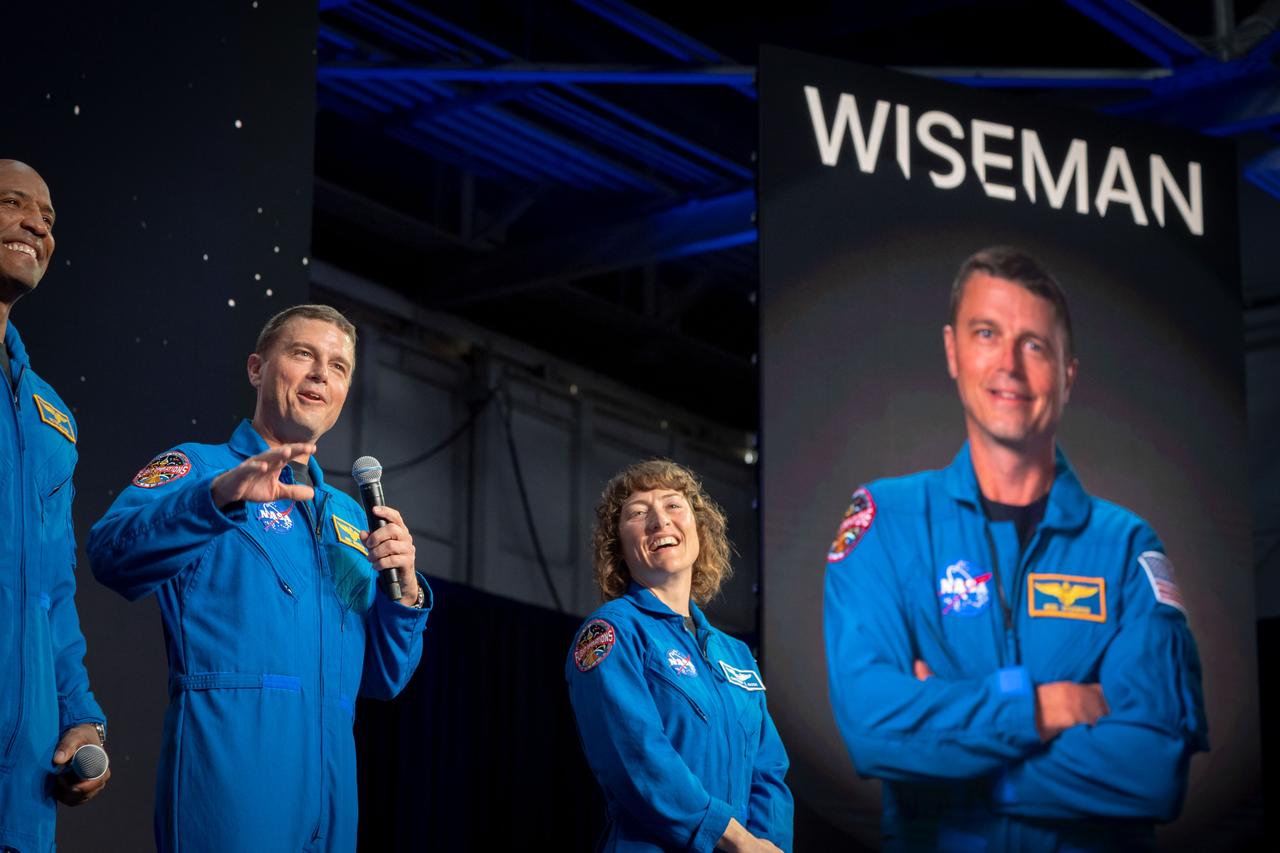 jsc2023e017444 (April 3, 2023) -- NASA astronaut Reid Wiseman addresses the crowd after being announced as one of four members of the Artemis II crew during a Monday, April 3, 2023, news conference at Ellington Field near NASA’s Johnson Space Center in Houston. The crew is comprised of Commander Reid Wiseman, Pilot Victor Glover, and Mission Specialists Christina Koch and Jeremy Hansen. The four astronauts will venture around the Moon on Artemis II, the first crewed mission on NASA’s path to establishing a long-term presence at the Moon for science and exploration through Artemis. Wiseman is joined on stage by Artemis II crew members from left, NASA astronauts Pilot Victor Glover and Mission Specialist Christina Koch.