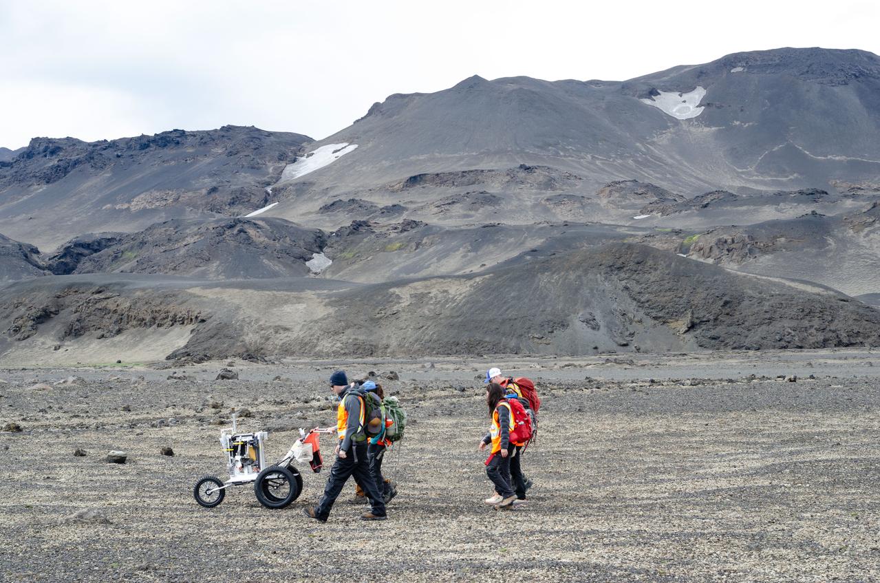jsc2023e041422 --- Artemis II science trainers push a lunar tool cart across the lunar-like landscape of Iceland during an Artemis II crew geology field training.