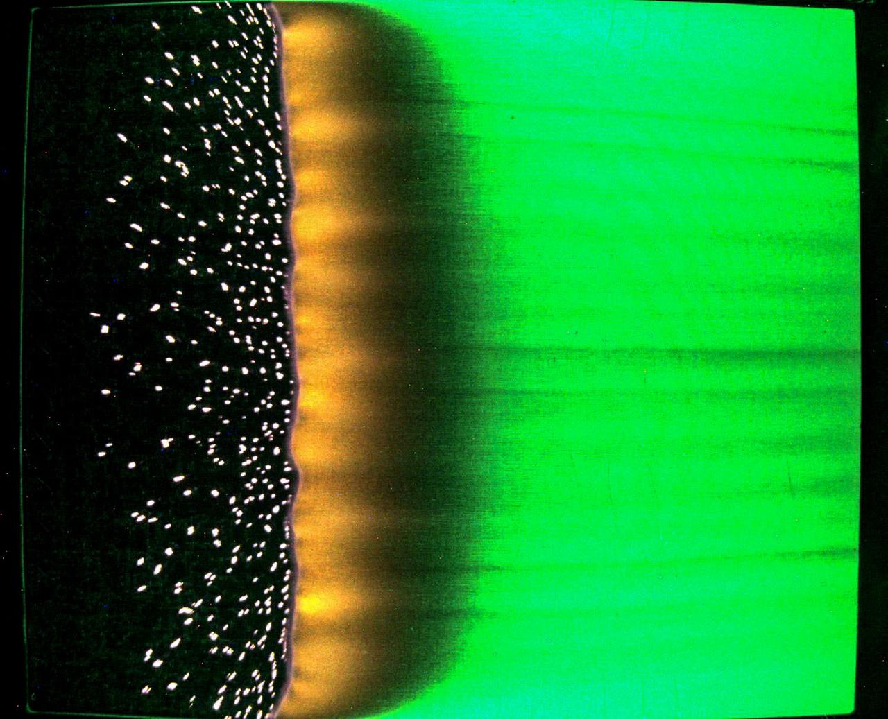 jsc2023e046375 (7/25/2023) --- A sample of fabric burns inside Spacecraft Fire Experiment-IV (Saffire-IV). The sample is a composite fabric made of cotton and fiberglass and is 40 cm wide. The image appears green because green LED lights are used to illuminate the sample during a burn. The flame appears orange in this image and the black region to the right of the flame is the cotton in the sample beginning to heat and char. The bright specks to the left of the flame are smoldering cotton that remains on the fiberglass substrate after the flame passes. In Saffire-VI, this fabric is burned at higher oxygen concentrations. Researchers aim to study realistic flame spread to aid the development of fire safety equipment and strategies for future spacecraft.