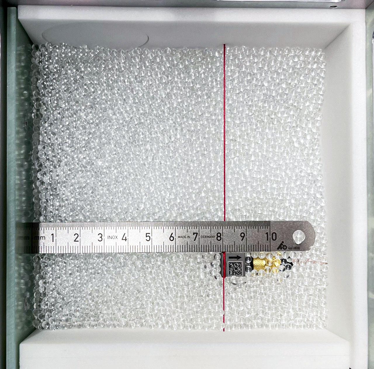 jsc2023e053546 (3/3/2023) ---    Granular Sound: open sample cell, partially filled with glass beads, with one accelerometer exposed whose position from the voicecoil-driven wall on the left is indicated by a metal ruler. Also visible: the sample cell walls are padded with foam for acoustic decoupling of the glass bead packing. Image courtesy of DLR-MP.