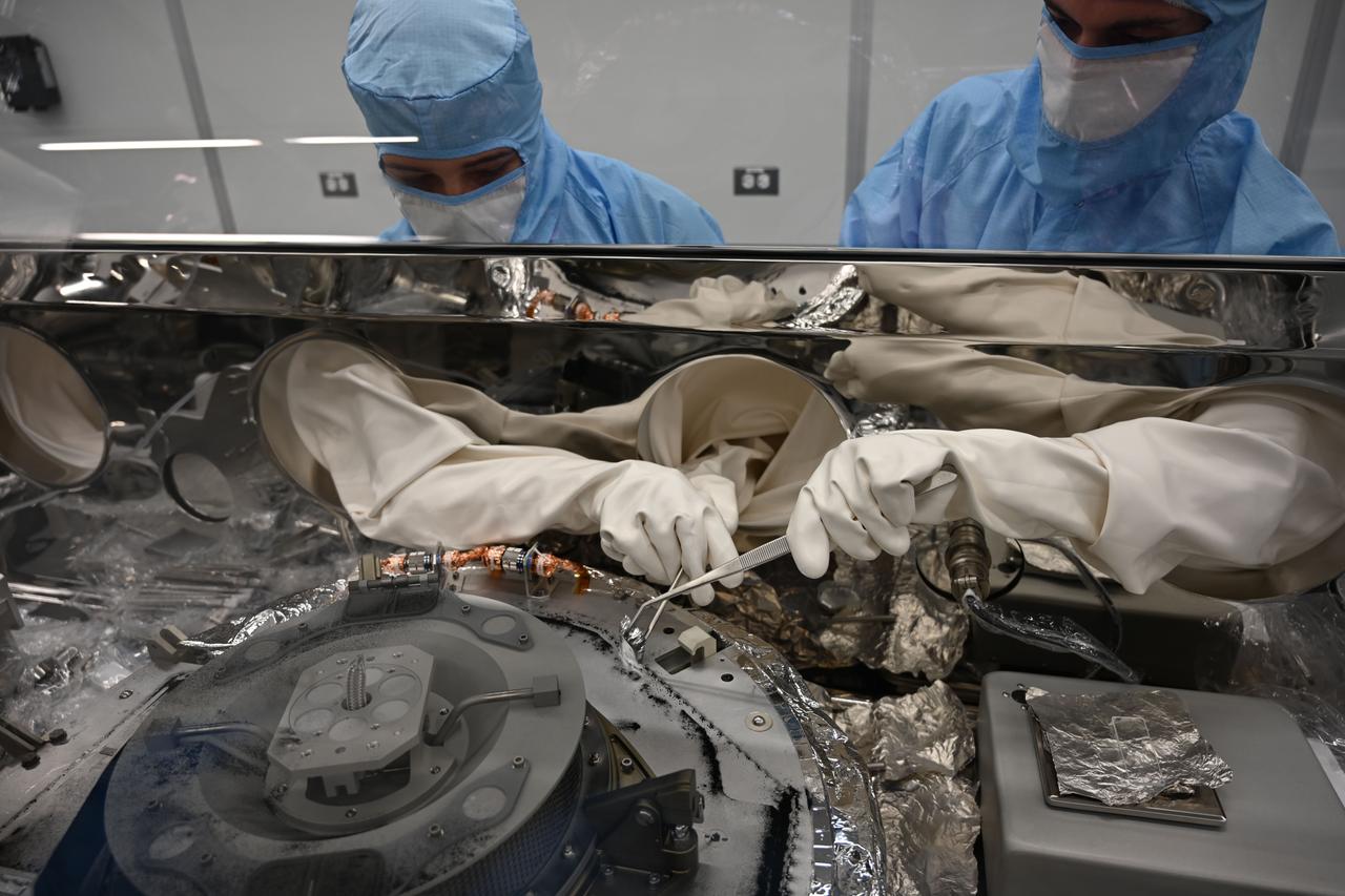 Astromaterials processors Mari Montoya, left, and Curtis Calva, right, use tools to collect asteroid particles from the base of the OSIRIS-REx science canister. Credit: NASA