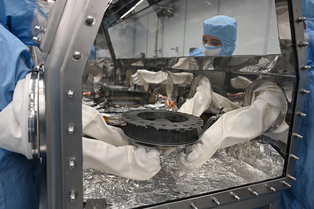 Astromaterials processor Mari Montoya and OSIRIS-REx curation team members set the TAGSAM (Touch and Go Sample Acquisition Mechanism) down in the canister glovebox after removing it from the canister base and flipping it over. Credit: NASA/ Kimberly Allums