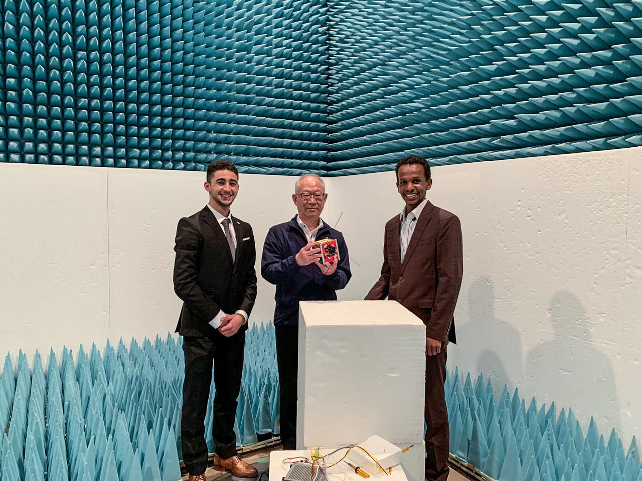 jsc2024e006082 (3/31/2022) --- MicroOrbiter Inc. Team standing in the Anechoic Chamber. The CEO is holding the Engineering Model between his hands.From left to right : MOUMNI Fahd CTO and Co-Founder, HIRAKATA Yoji CEO and Founder, ABBAS Yasir CDO...Image Credit: MOUMNI Fahd.