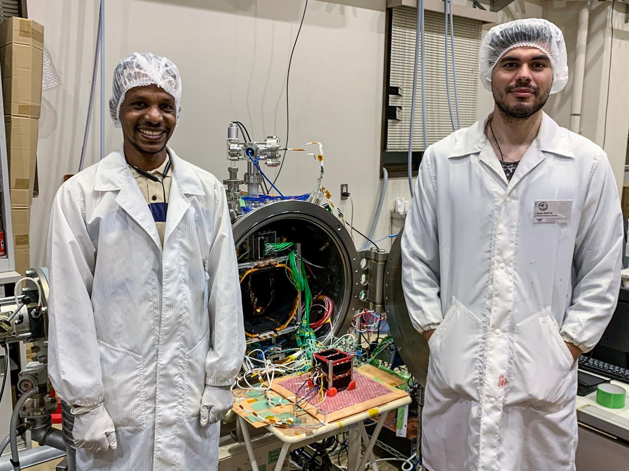 jsc2024e006087 (10/5/2022) --- The thermocouples needed for measurements are connected to the flight model before conducting the thermal vacuum test.Two members are standing in front of the satellite and the chamber. From left to right : ABBAS Yasir, and MATTEI Giulio..Image Credit: MOUMNI Fahd.