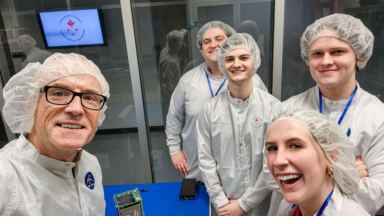 jsc2024e016246 (11/27/2023) --- Selfie of Killick-1 Satellite Integration Team in the Canadian Space Agency Clean Room with the Killick-1 satellite (foreground). From left to right – Desmond Power (Co-Principal Investigator), Matthew Fewer (Computer Engineering Student), Cameron King (Computer Engineering Student), Victoria Vaters (Mechanical Engineering Student), Daniel Dolomount (computer Engineering Student). Nanoracks-Killick-1 is a CubeSat that measures sea ice parameters using Global Navigation Satellite System (GNSS) reflectometry or reflected signals. Image courtesy of C-CORE and Memorial University.