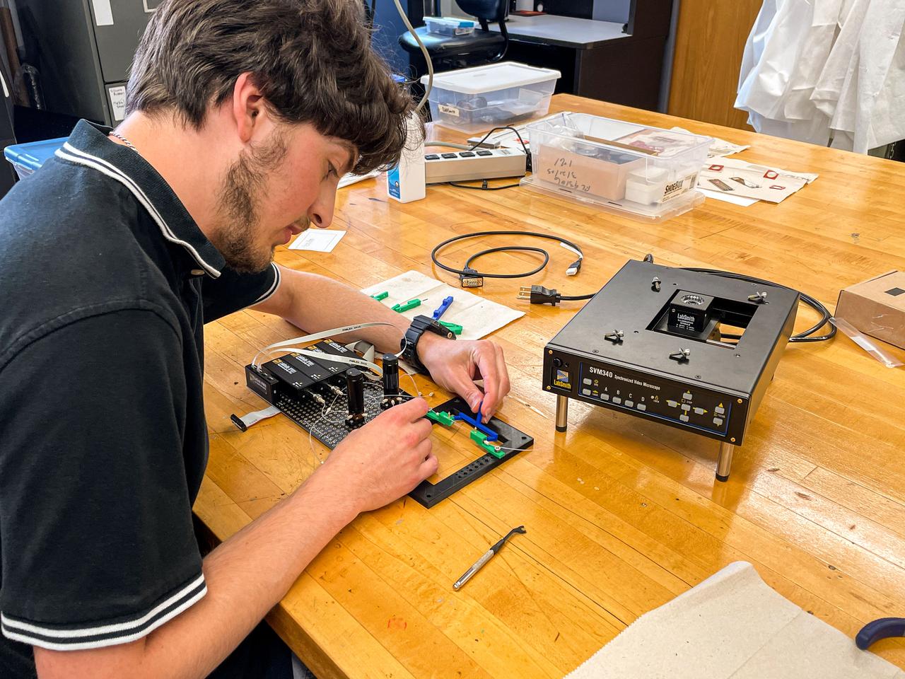 jsc2024e016254 (7/30/2021) --- A capstone student assembles the microscope and fluid breadboard for the Nano Particle Haloing Suspension payload. This payload tests controlled assembly of nanoparticles in a solution of zirconia and titanium-dioxide coated silica. Effective demonstration could lead to applications in an enhanced solar cell generation technology known as quantum-dot solar synthesis. Image courtesy of the University of Louisville.