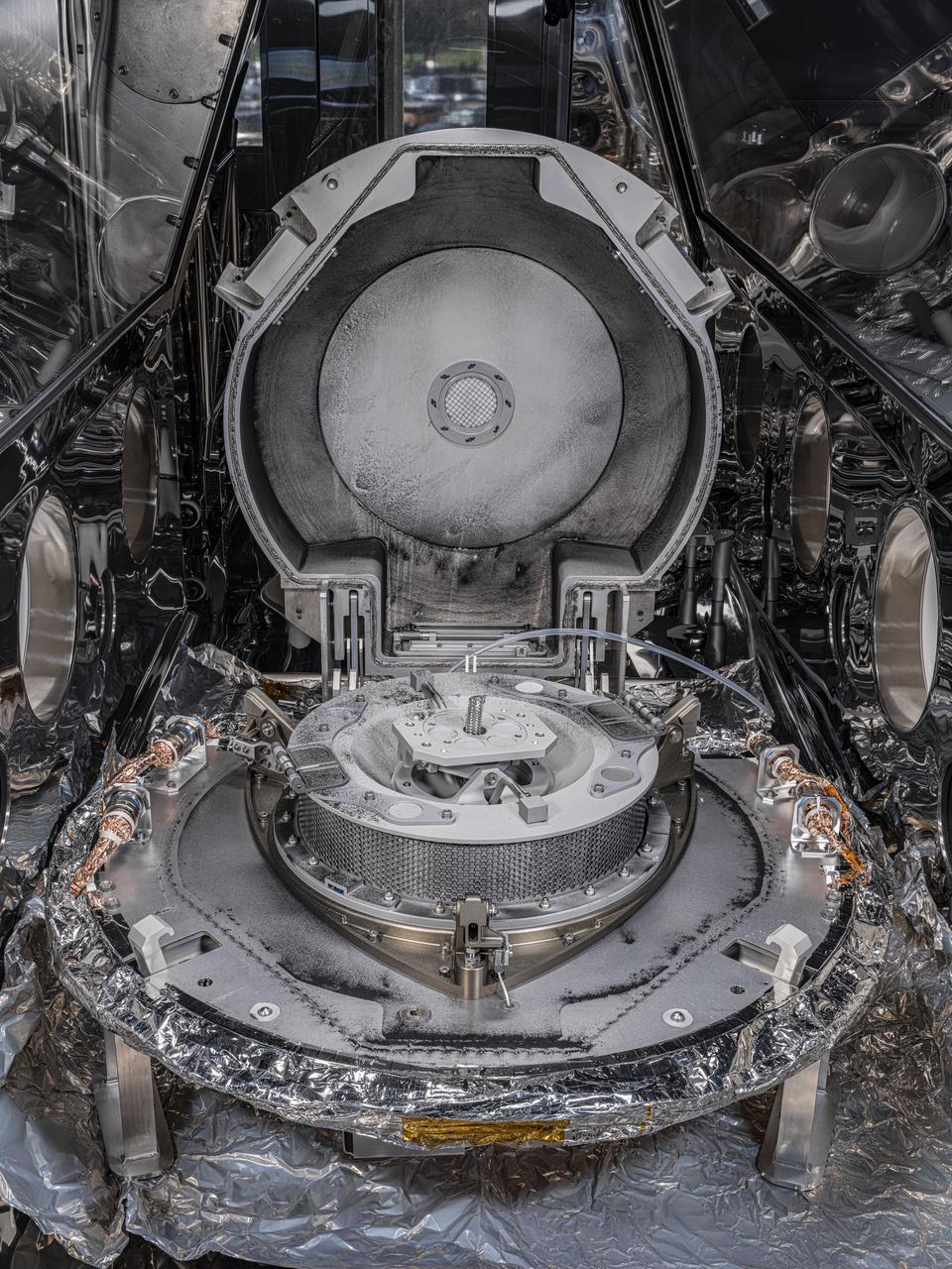 A view of the OSIRIS-REx sample canister with the lid removed, revealing the Touch and Go Sample Acquisition Mechanism (TAGSAM) inside. When astromaterials processors removed the canister lid, they discovered a coating of fine asteroid dust and sand-sized particles covering the inside of the lid and on the top of the avionics deck. The round portion in the center of the lower part of the canister is the TAGSAM that was used to collect pristine material from asteroid Bennu in 2020. The spacecraft delivered the sample return capsule to Earth on Sept. 24, 2023. OSIRIS-REx is the first U.S. mission to collect a sample from an asteroid. Scientists hope the Bennu sample will reveal whether asteroids that collided with Earth billions of years ago thereby delivered water and other ingredients for life to our planet.    Credits: Photo credit: NASA/Erika Blumenfeld & Joseph Aebersold    Image Capture: Created using manual high-resolution precision photography and semi-automated focus stacking procedure.