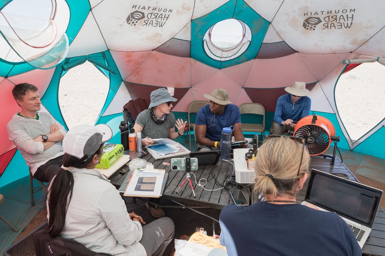 NASA astronauts Kate Rubins and Andre Douglas meet with teams to review test objectives and traverse plans before their first simulated moonwalk in a week-long field test consisting of four simulated moonwalks and six advanced technology runs in the San Francisco Volcanic Field in Northern Arizona on May 13, 2024.  Credit: NASA/Josh Valcarcel 