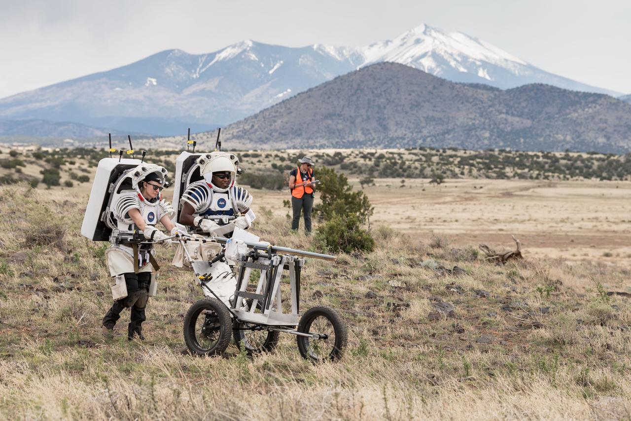 NASA astronauts Kate Rubins and Andre Douglas push a tool cart loaded with lunar tools through the San Francisco Volcanic Field north of Flagstaff, Arizona, as they practice moonwalking operations for Artemis III on May 13, 2024.   Credit: NASA/Josh Valcarcel 